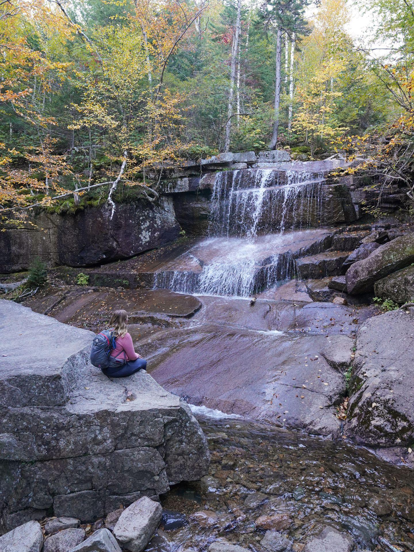 Lydia sitting on a large rock and looking at a small waterfall.