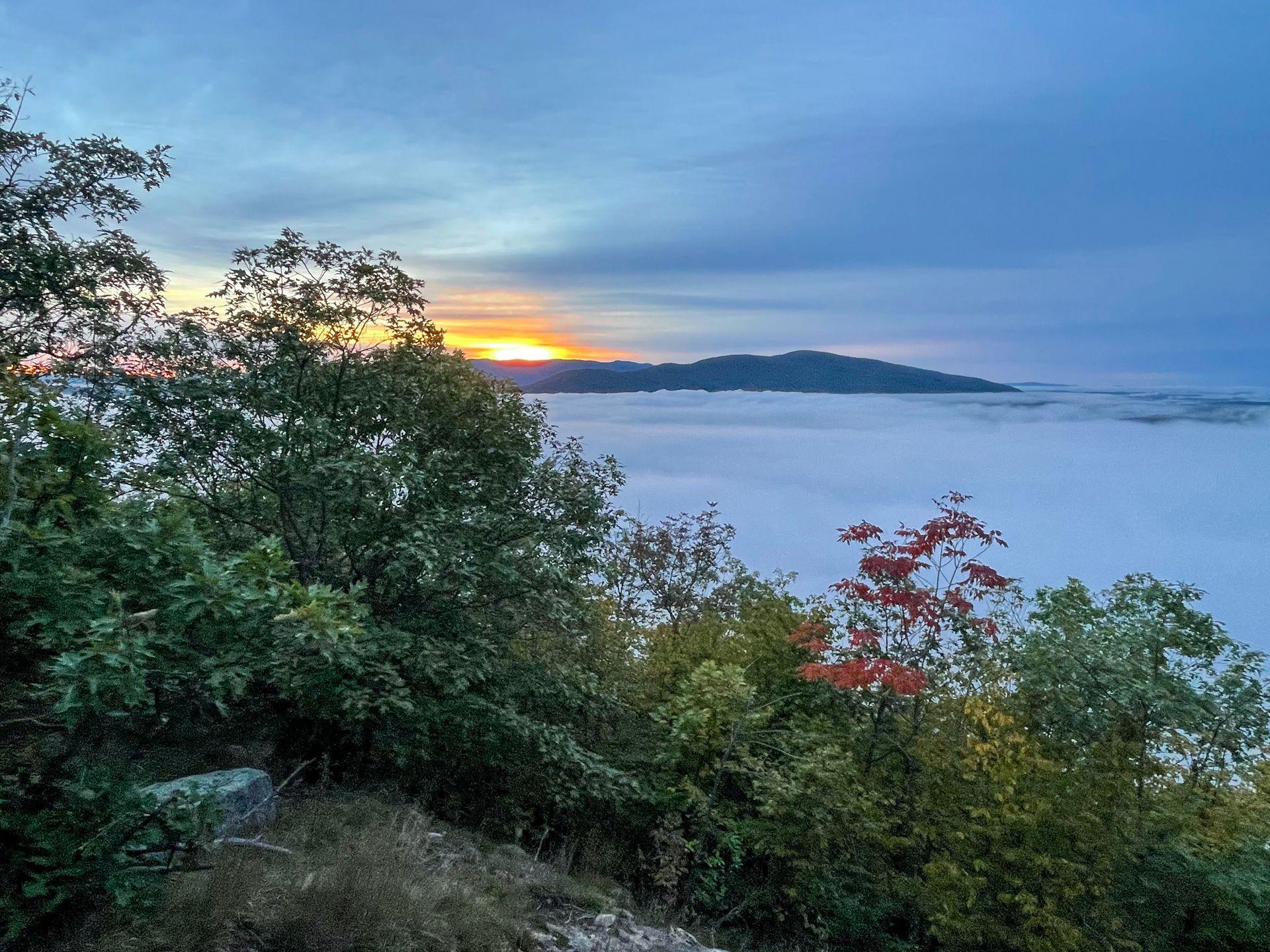 A cloud inversion from the East Rattlesnake Trail. The sun rises over a mountain in the distance.