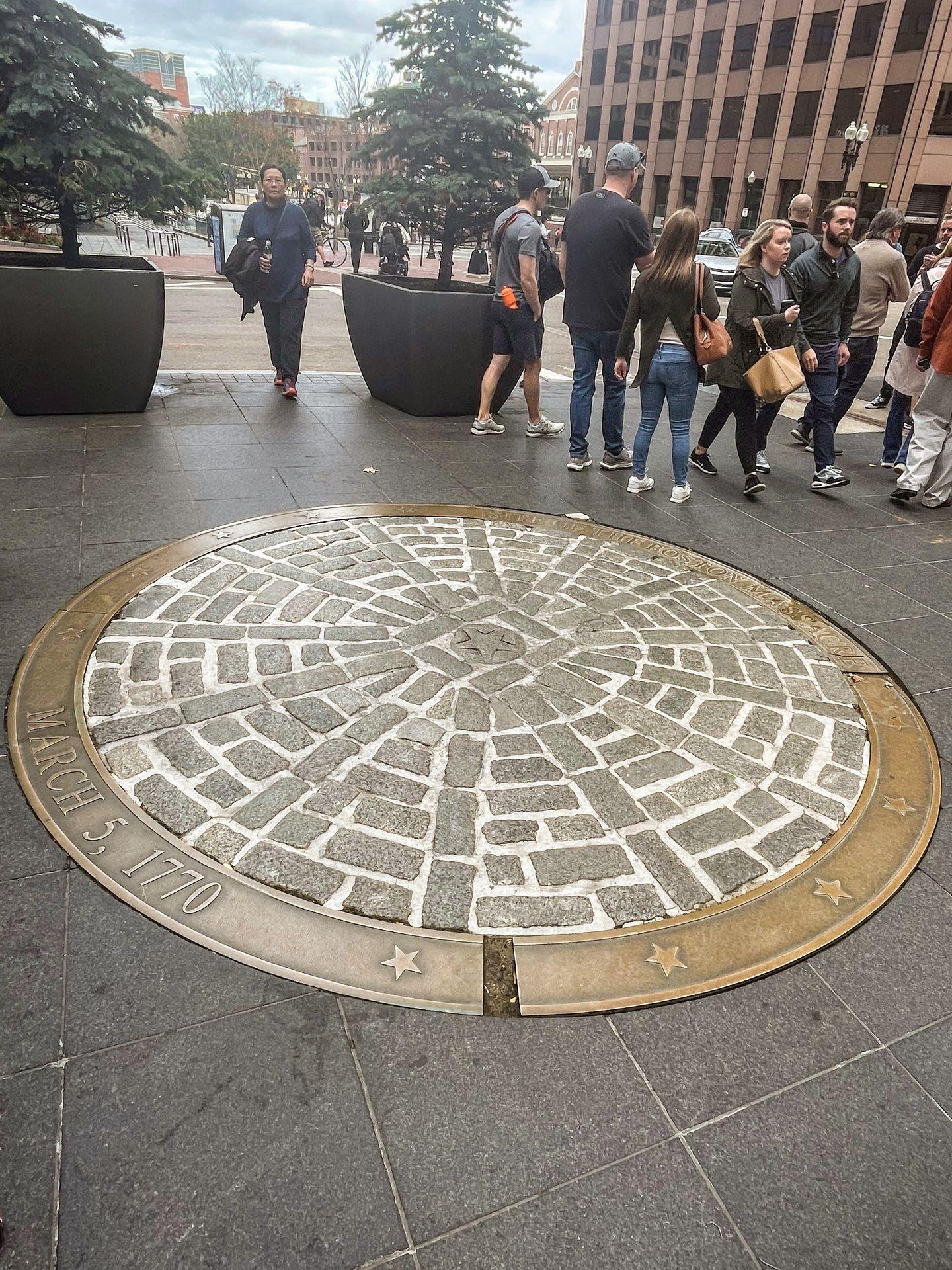 A large plague on the ground representing the place where the Boston Massacre occurred. The site is round and features bricks with a gold rim.