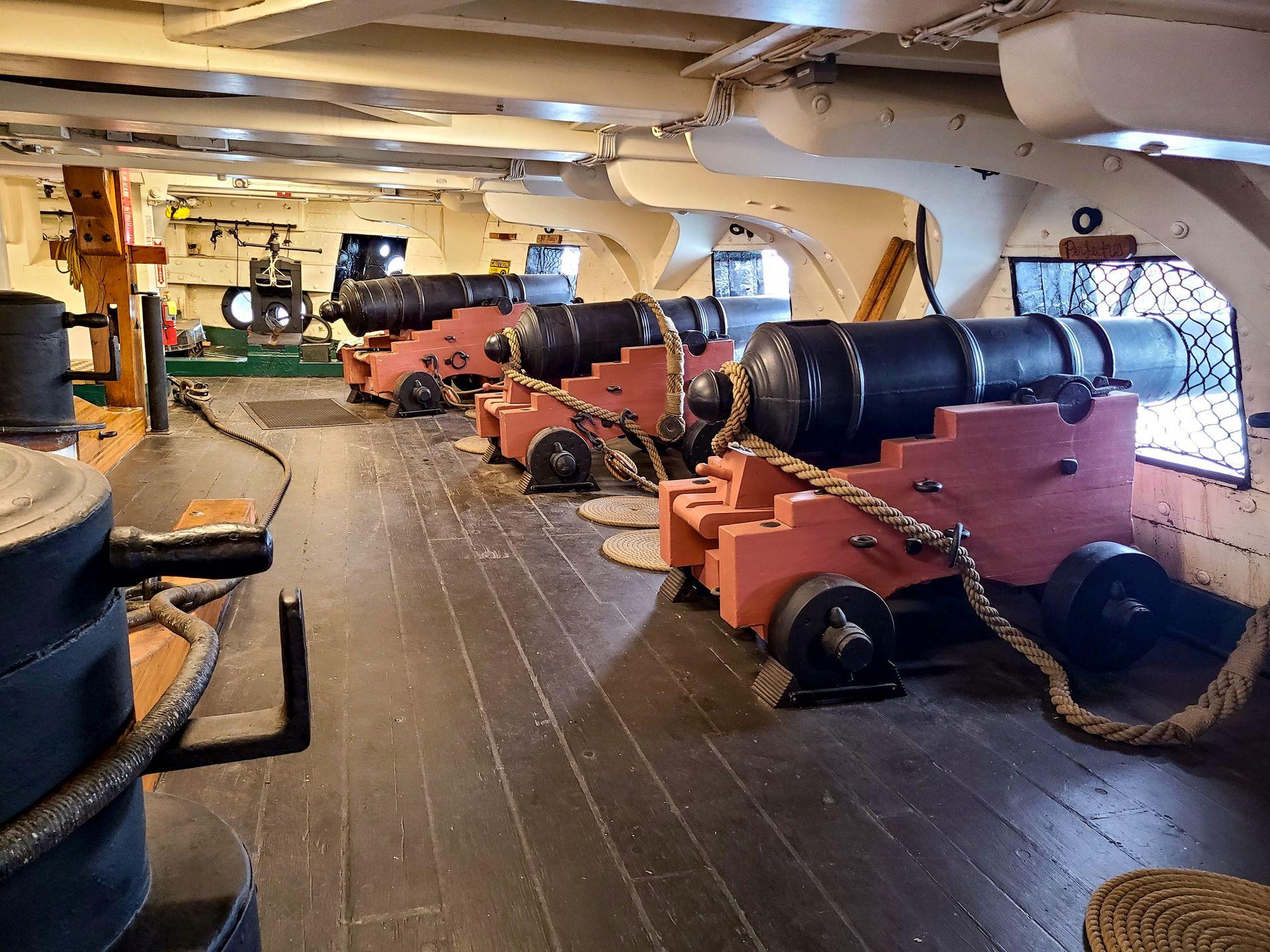 Several cannons pointing out windows inside of the USS Constitution