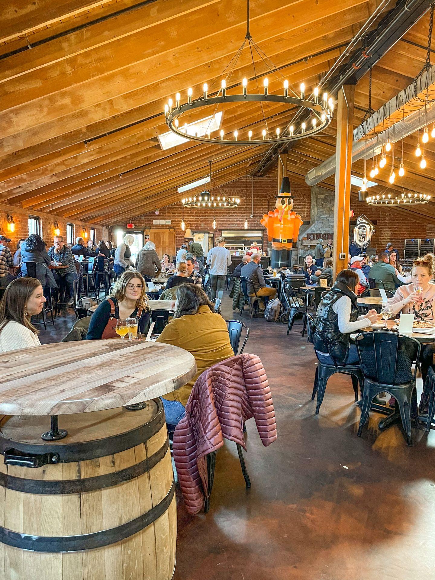 The interior of Kinsmen Brewing. There is a table made from a barrel, round light fixtures and a lot of wood in the details.