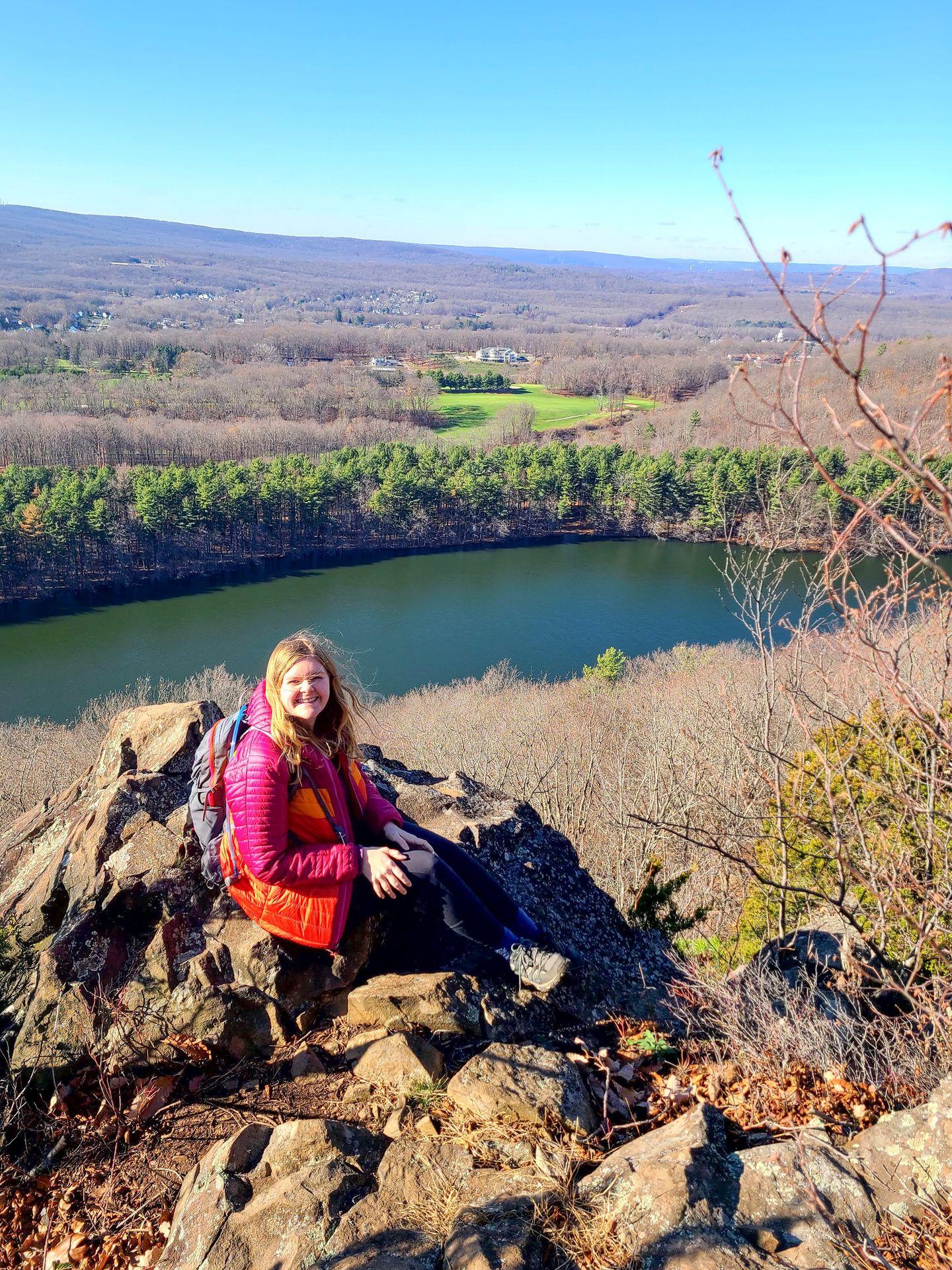 Taken from the top of Chauncey Peak, Lydia sits on a rocky area with views of the lake and the surrounding valley behind her.