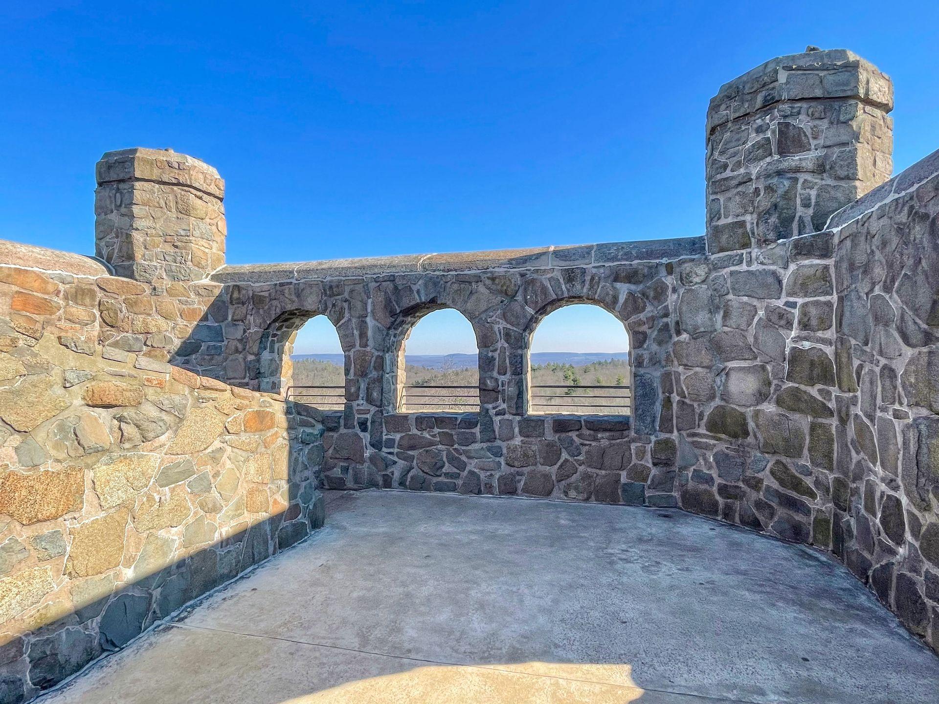 Inside the top of the tower at Sleeping Giant State Park. The building is made of stone and there are 3 windows that show a view of the area.
