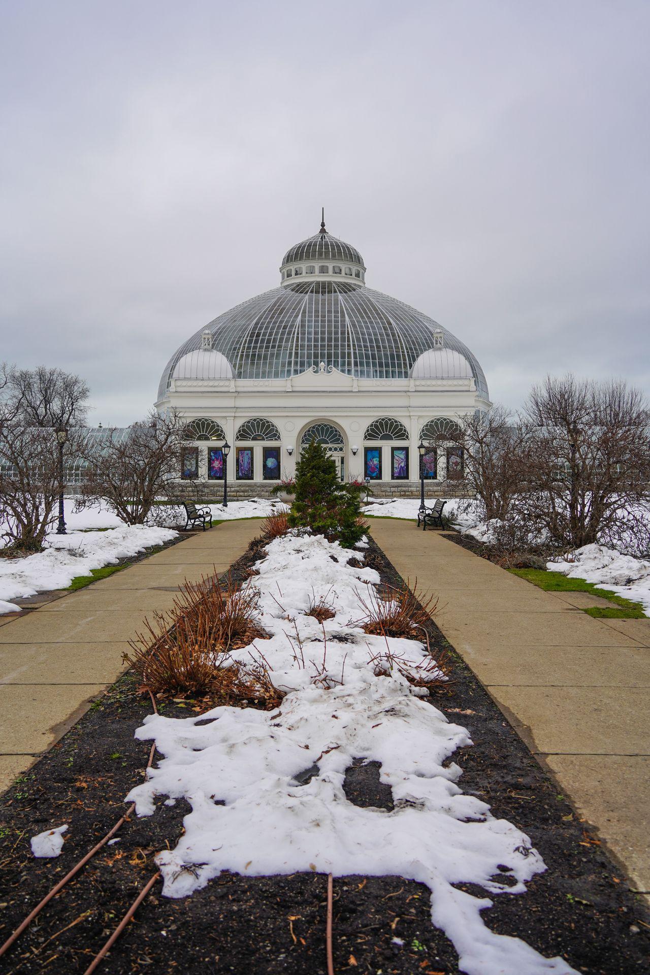 Looking straight at the Buffalo Botanical Gardens builidng, which is a glass greenhouse. There is a bit of snow on the ground on top of the garden beds outside of the building.