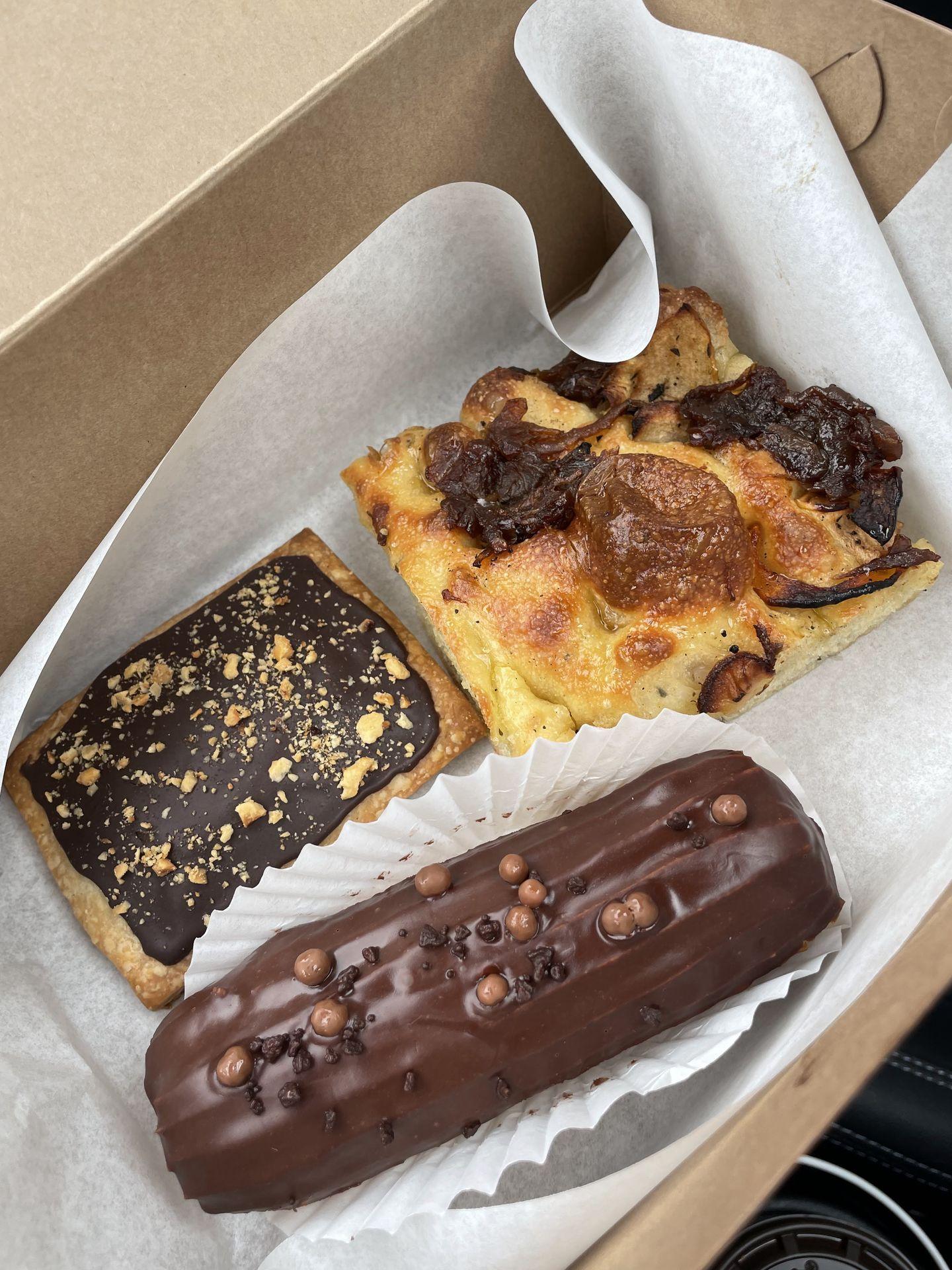 Three pastires in a to-go box. There is a chocolate eclair, a chocolate pop tart and focaccia bread.