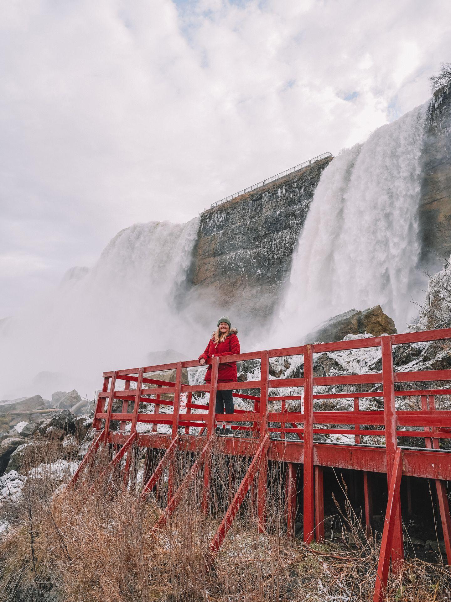 Lydia standing next to a red fence and wearing a red jacket at Cave of the Winds in Niagara Falls.