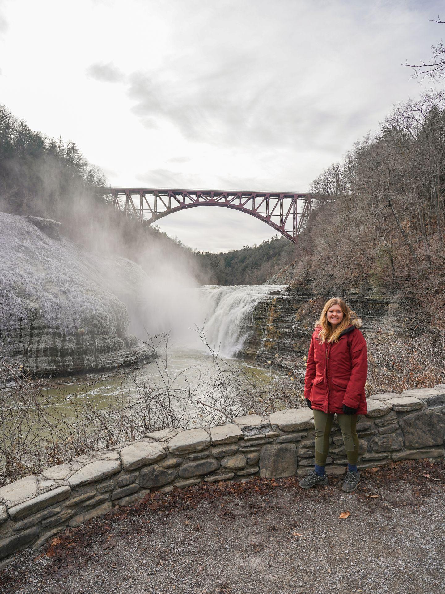 Lydia standing in front of a waterfall that has a bridge over it. There is a light dusting of snow and ice covering the rock face.