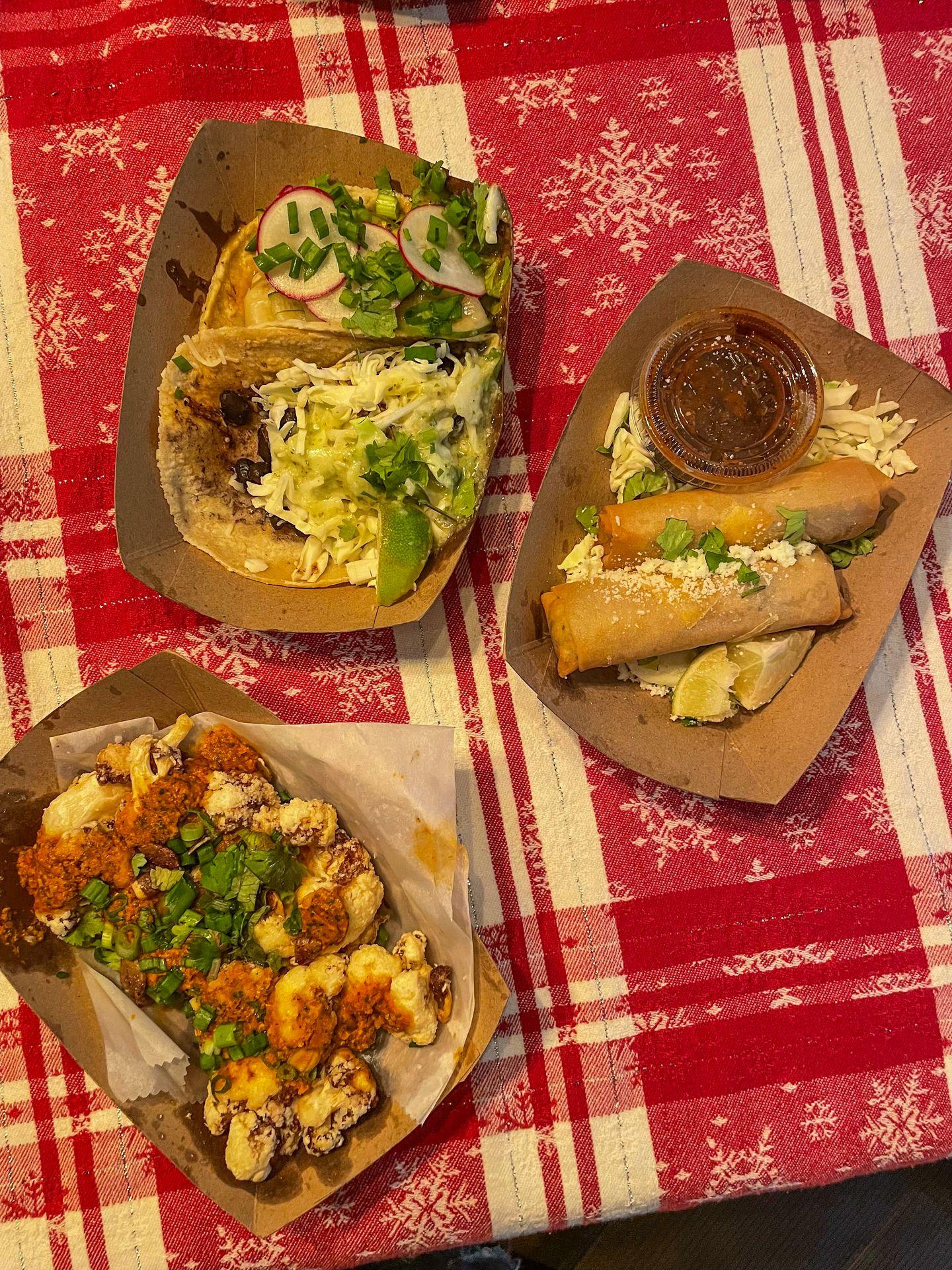 Three paper plates with cauliflower, egg rolls and tacos from Lloyd Taco Factory.