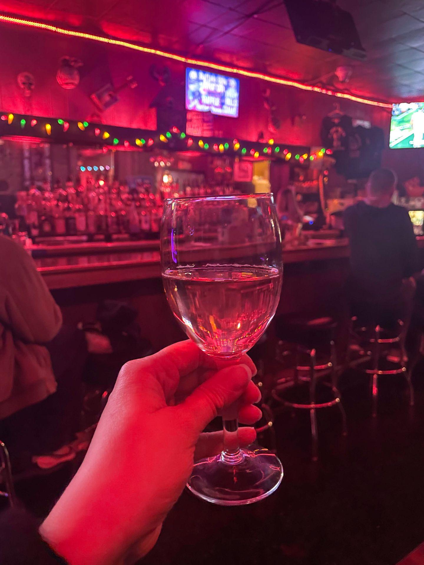 Holding up a glass with wine inside of a dimly lit bar with red lights.