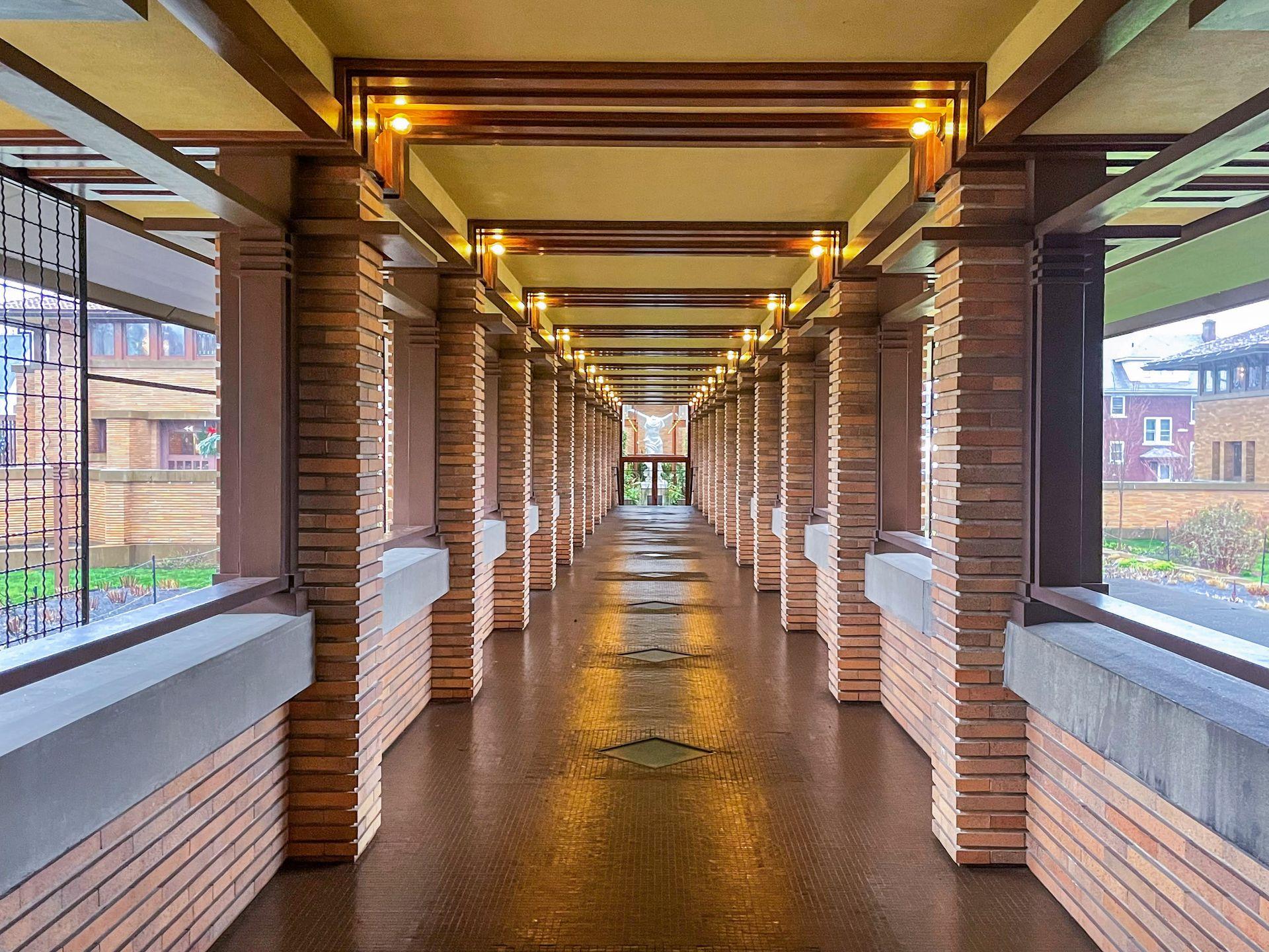 A partially outdoor hallway lined with brick pillars. At the end of the hallway is a white statue.