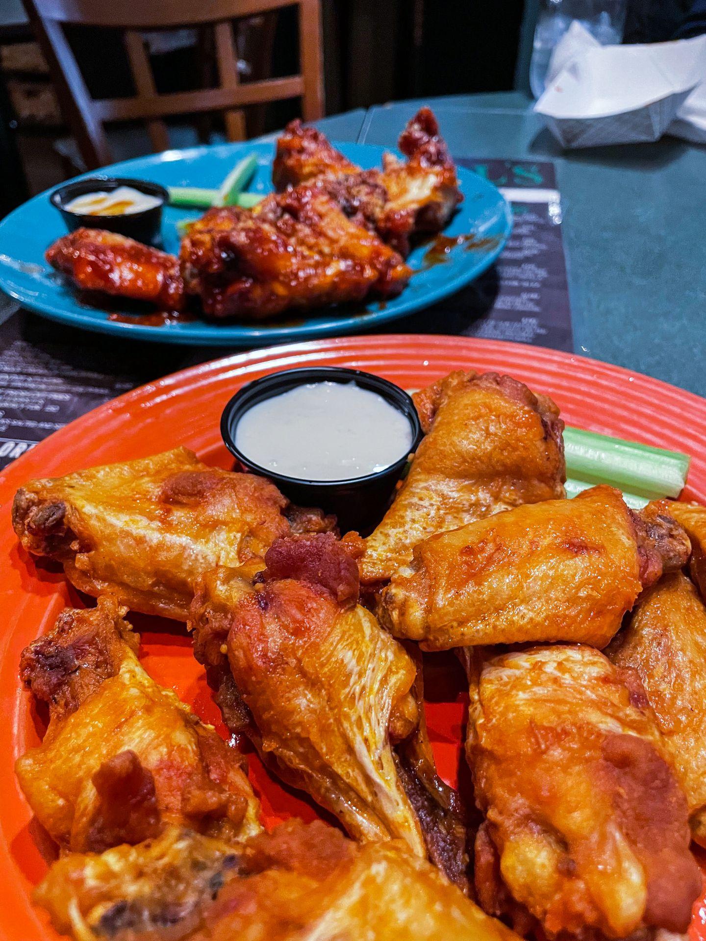 Two plates of chicken wings that include celery and a white dipping sauce.