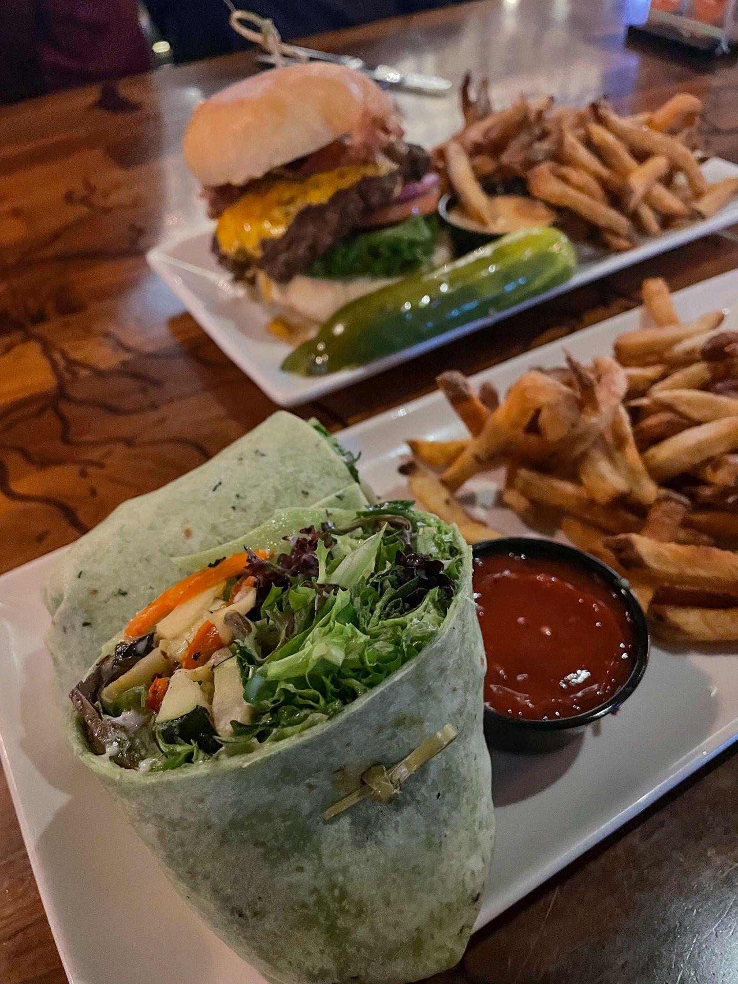 A plate of green wrap next to french fries. In the background there is a plate with a burger and fries.