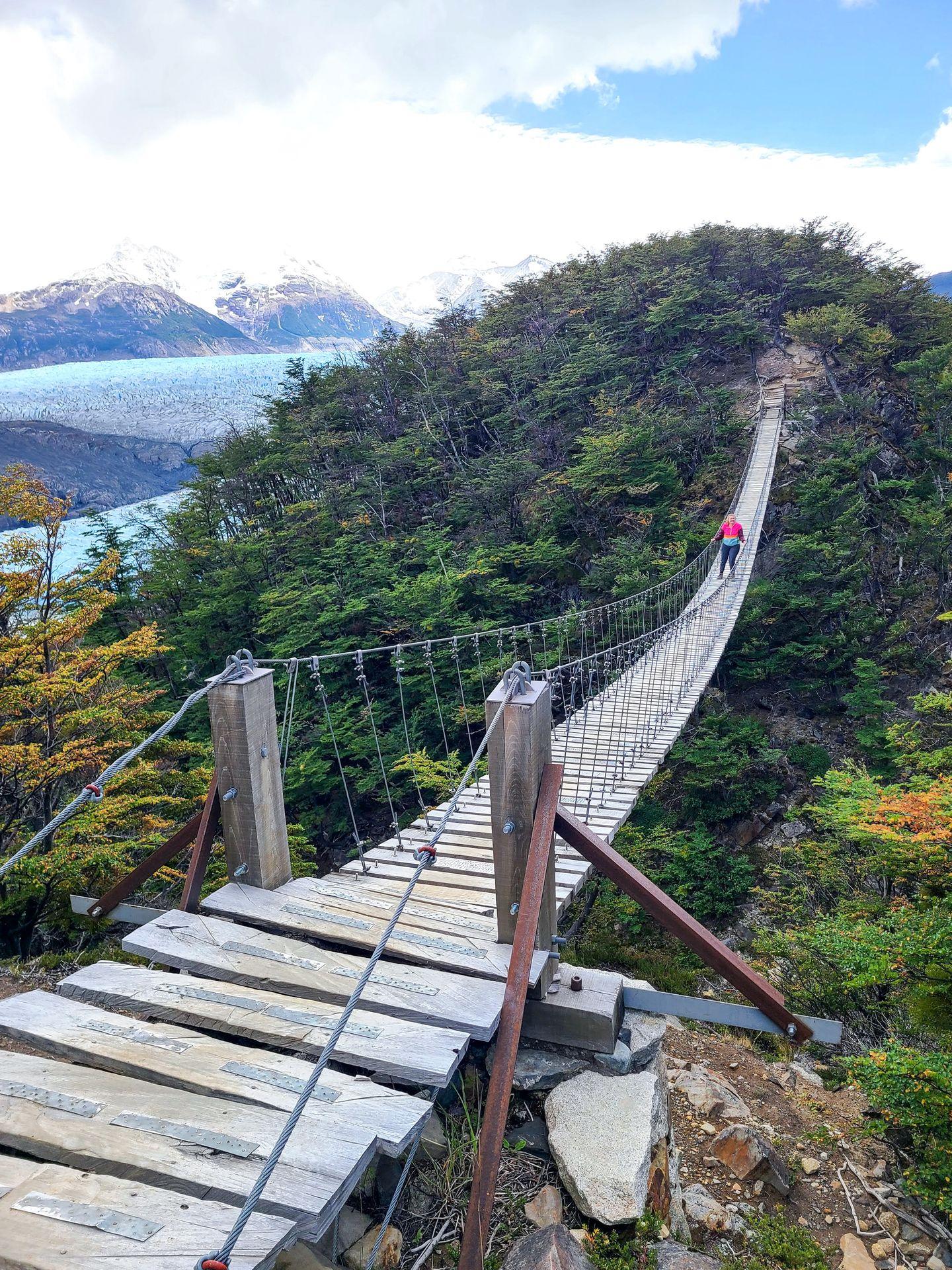 Lydia standing in the middle of a long suspension bridge. In the background, you can see the Grey Glacier.
