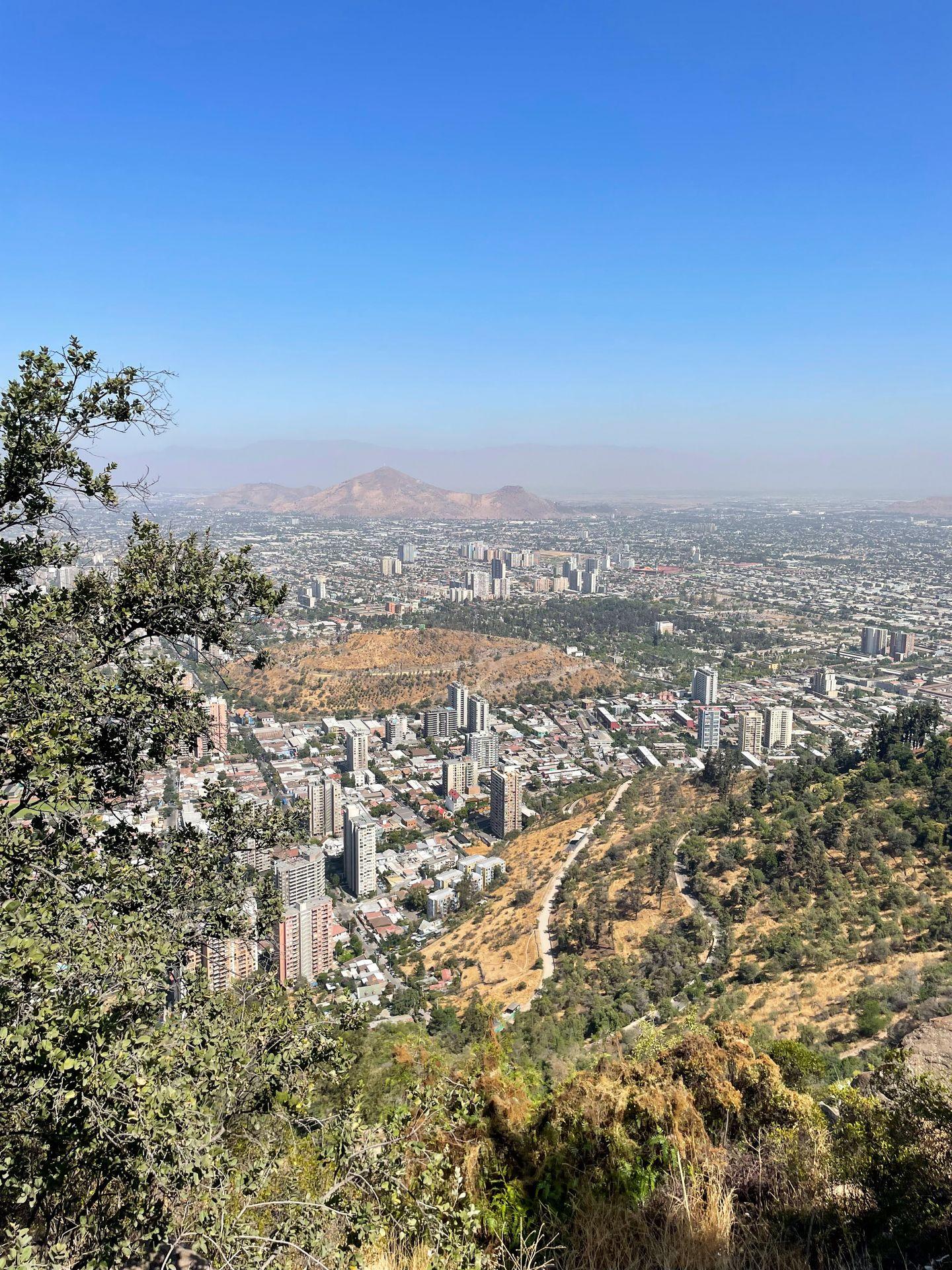 Looking down from a mountain at the city of Santiago. There is a mix of skyscrapers and shorter buildings.
