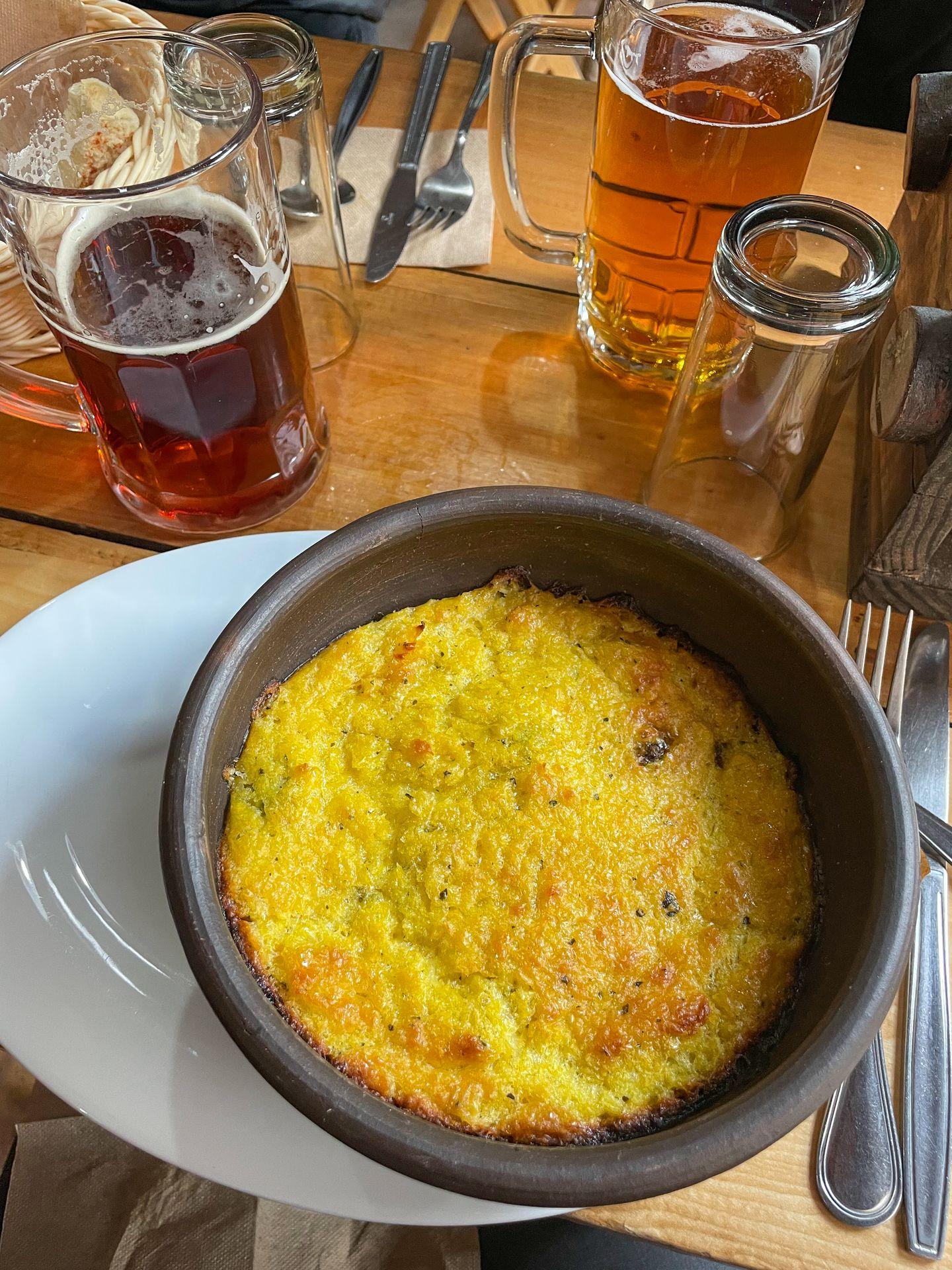 A bowl of a cornbread dish served for dinner at El Chileno. Large glasses of beer also sit on the table.