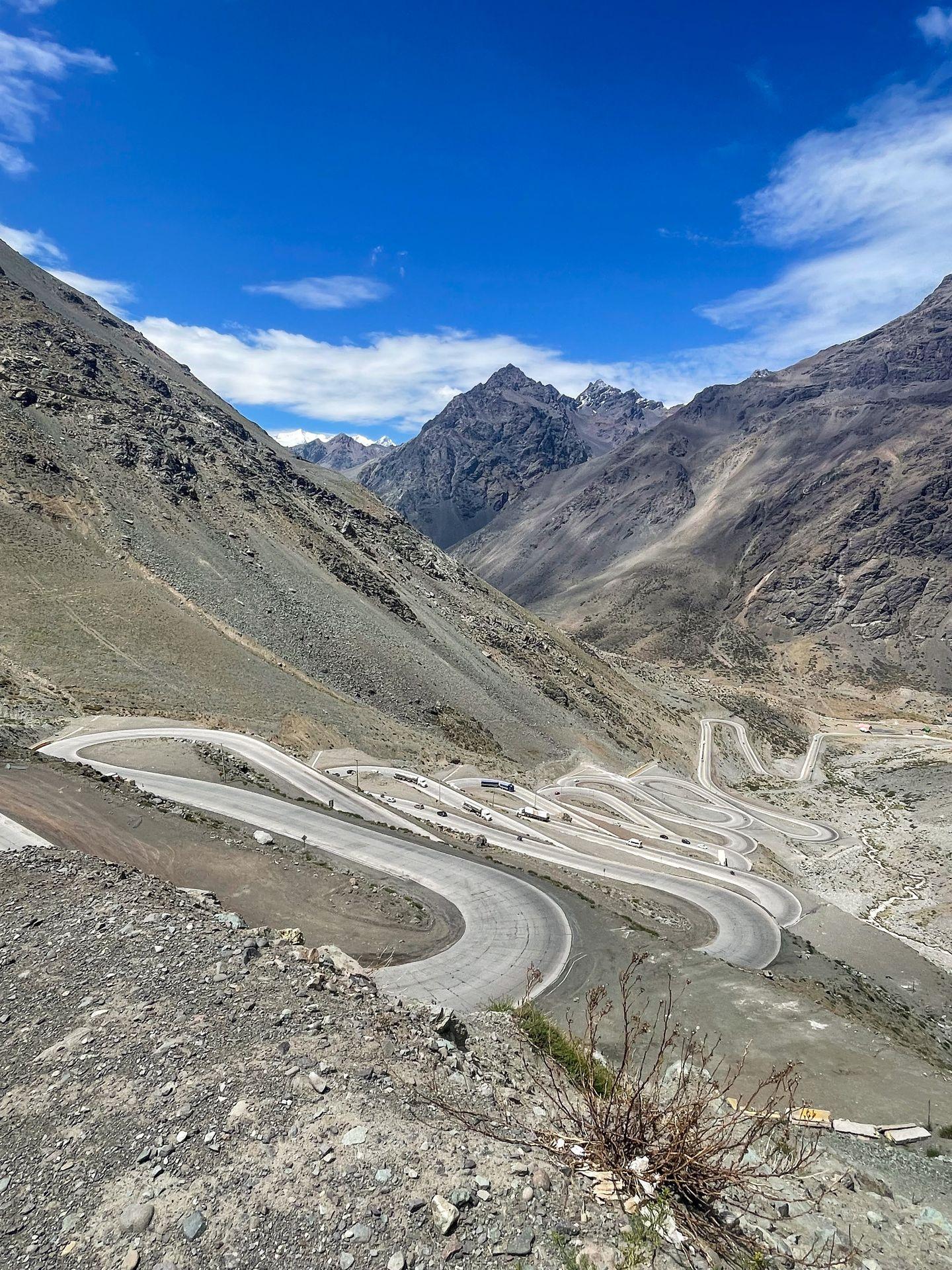 A road with several hairpin swithbacks and mountains in the distance.
