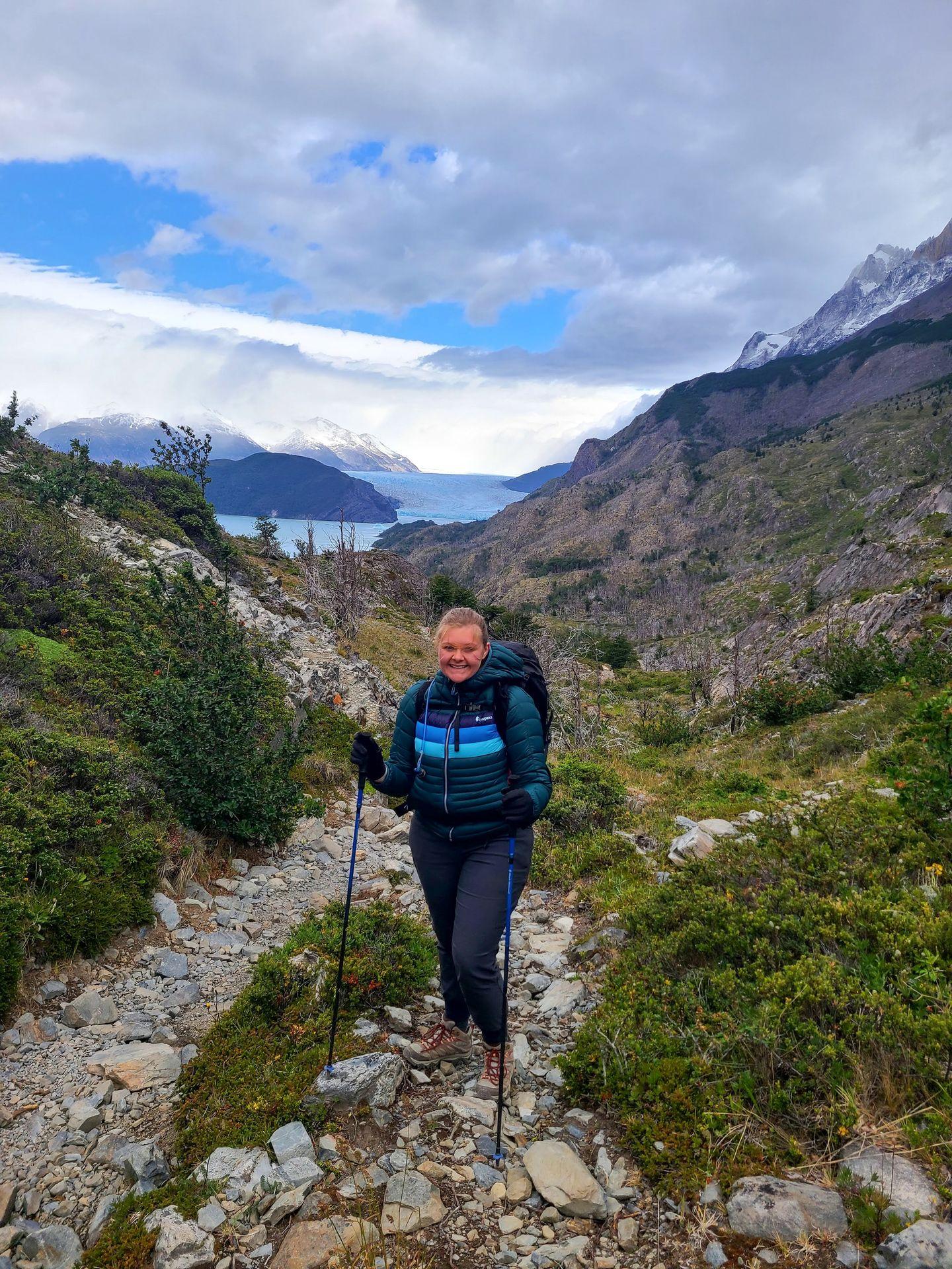 Lydia standing on a hiking trail with a view of the Grey Glacier in the distance.