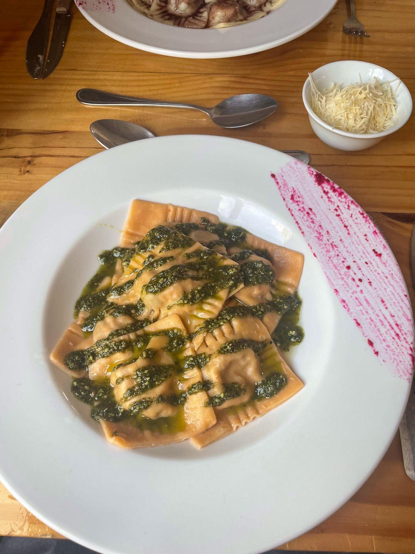 A plate of ravioli drizzled with a green sauce. There is also a bit of purple sauce used as decoration.