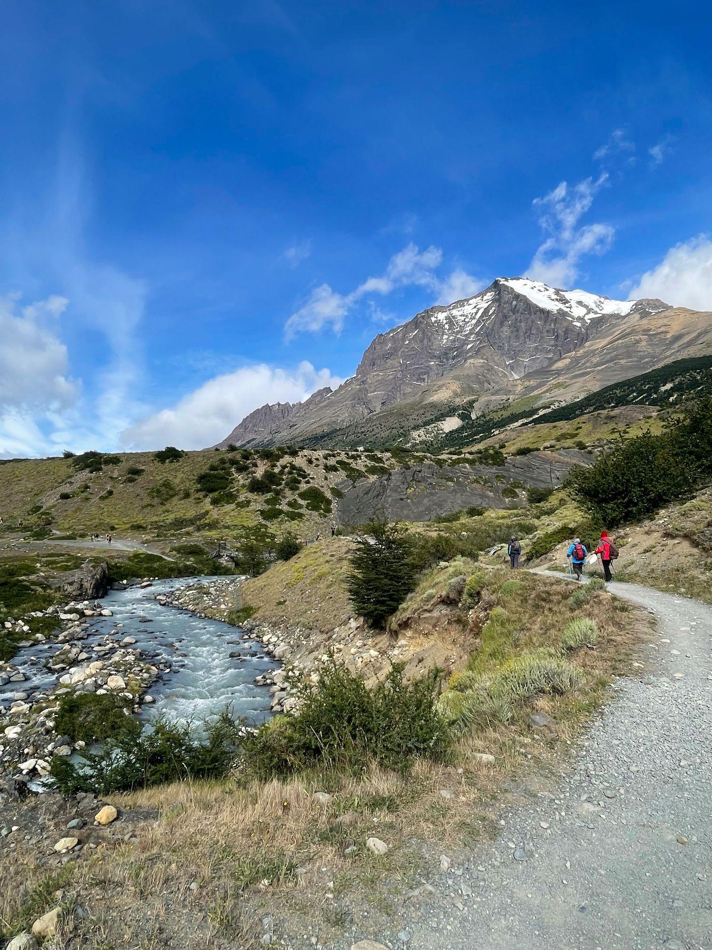 A flat trail next to a curving river with a mountain in the background.