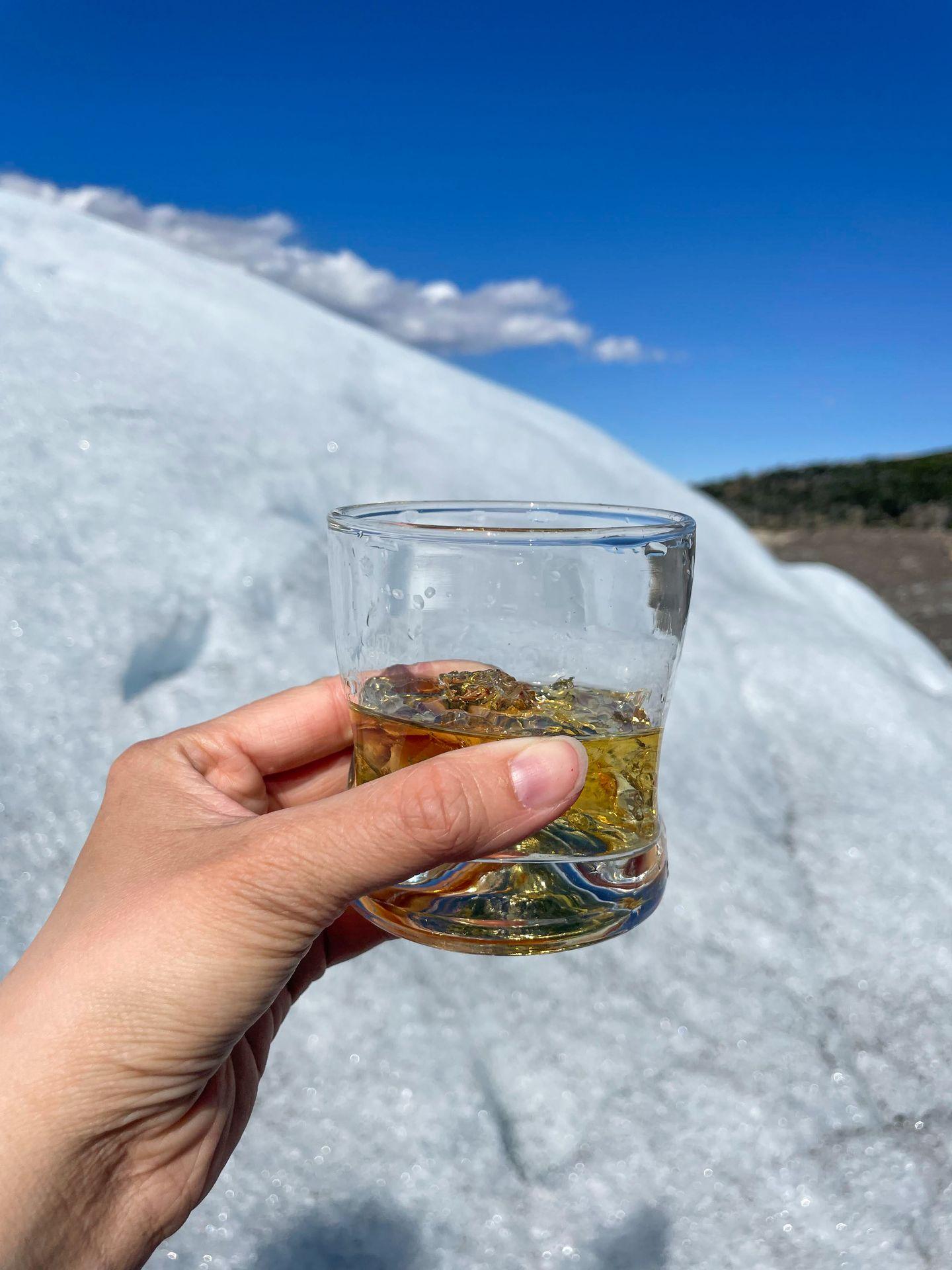 Holding up a glass of whiskey while on a glacier.