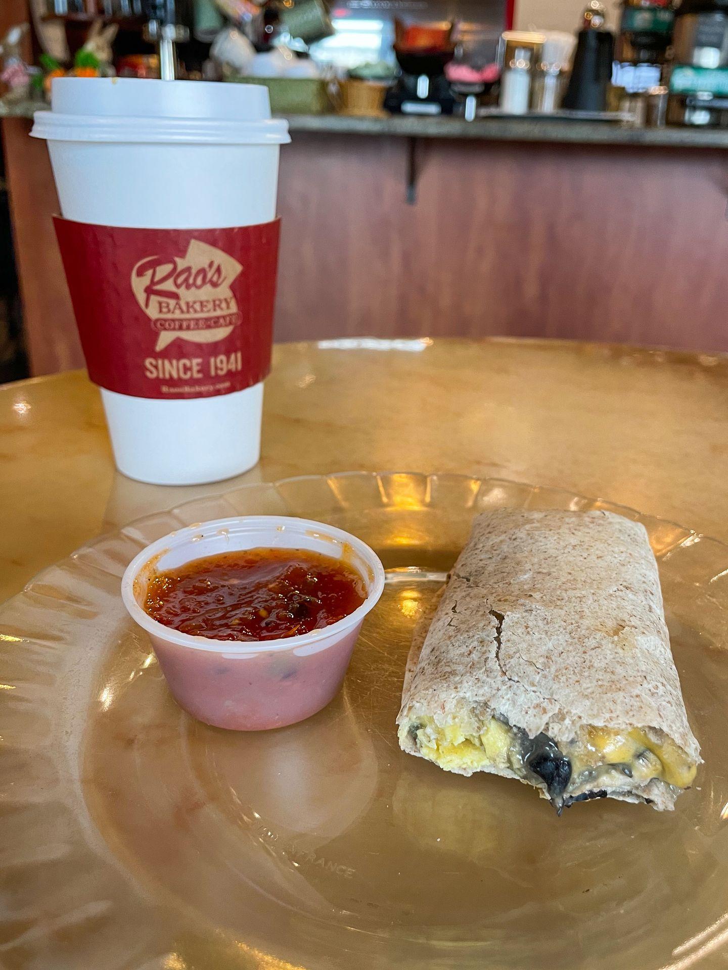 A half eaten breakfast burrito next to a cup of salsa at Rao's