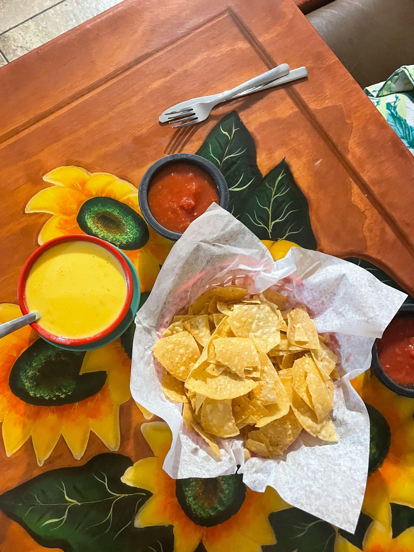 A bowl of chips next to salsa and queso sitting on a colorful table.