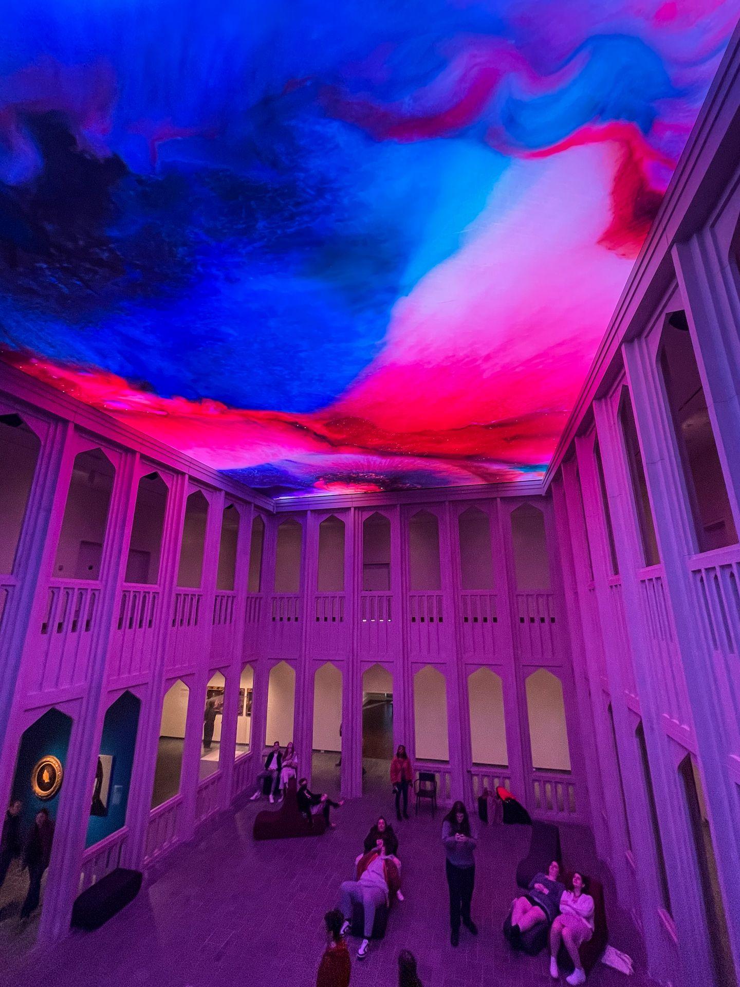 A large room with a ceiling projected in abstract blue and red colors at the Newfields Museum of Art.