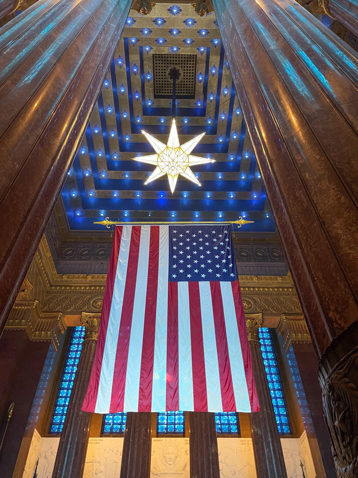 Looking up at an American flag and a tall room with giant pillars at the Indiana War Memorial.