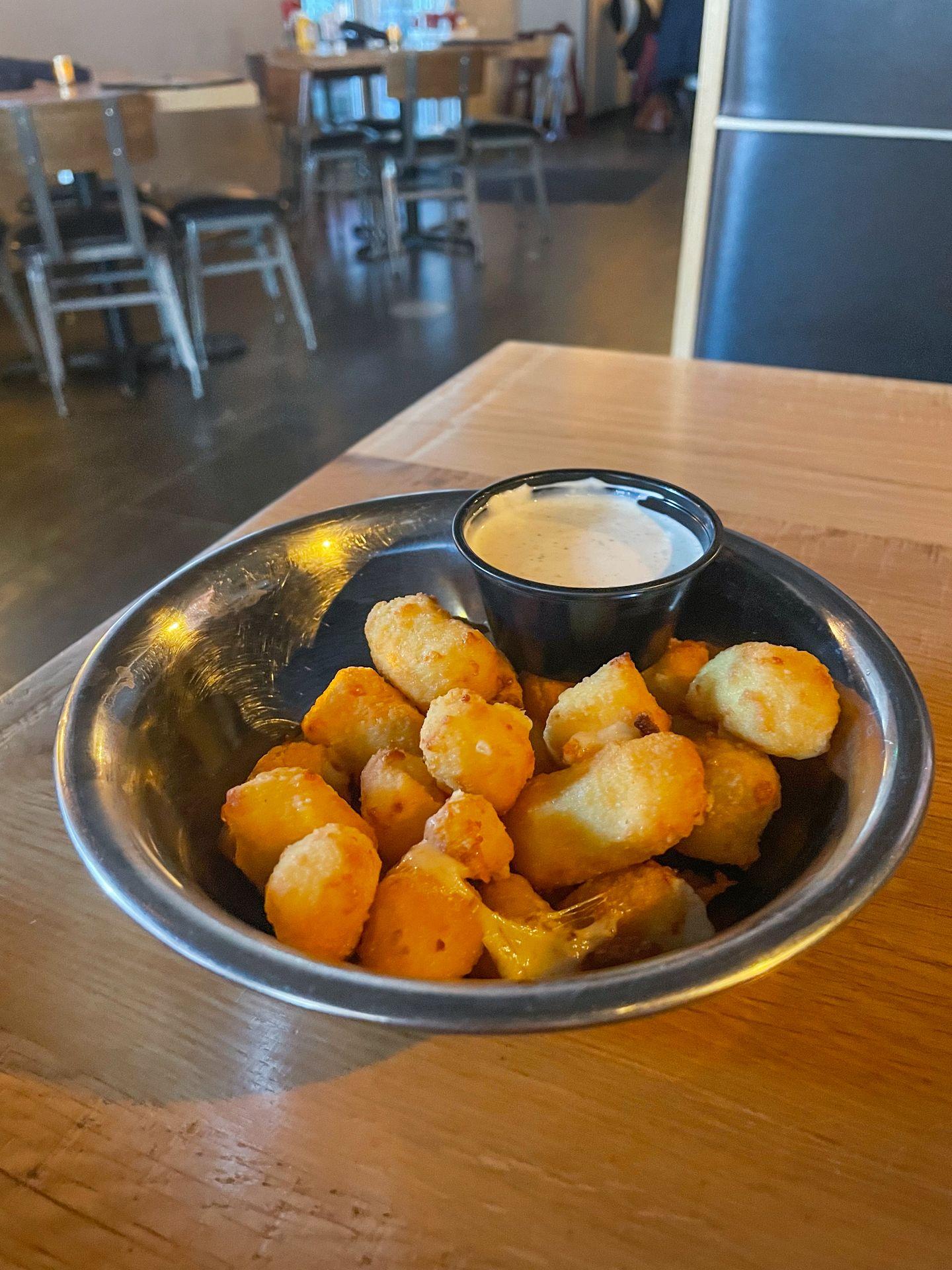 A silver bowl full of cheese curds with a ranch dipping sauce at Vintage Brewing