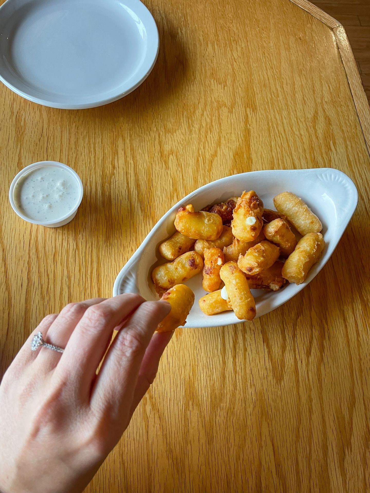 Looking down at a hand picking up a fried cheese curd from a dish in the Grumpy Troll Brew Pub