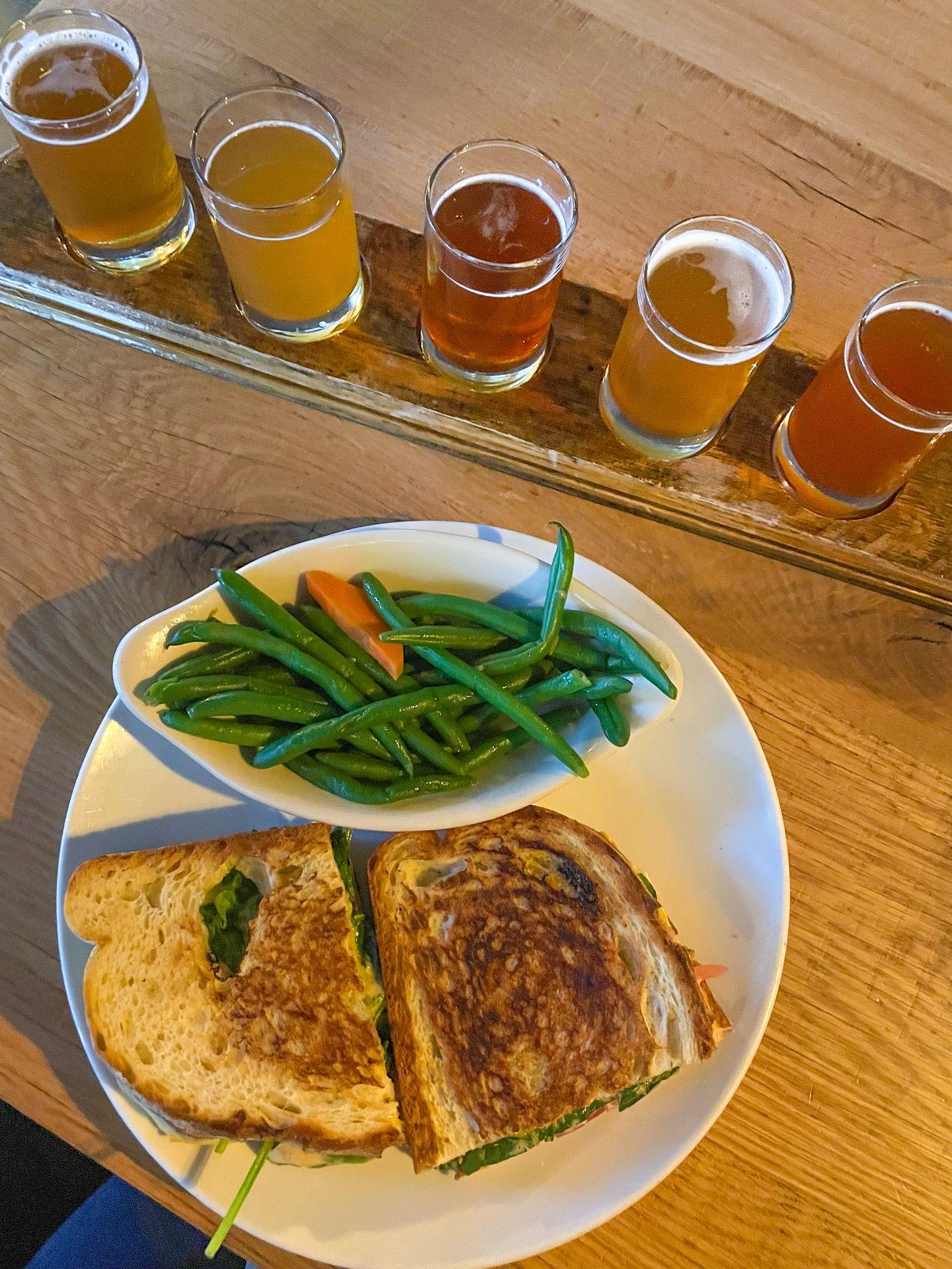 A panini with a side of green beans next to a flight of 5 beers from Vintage Brewing