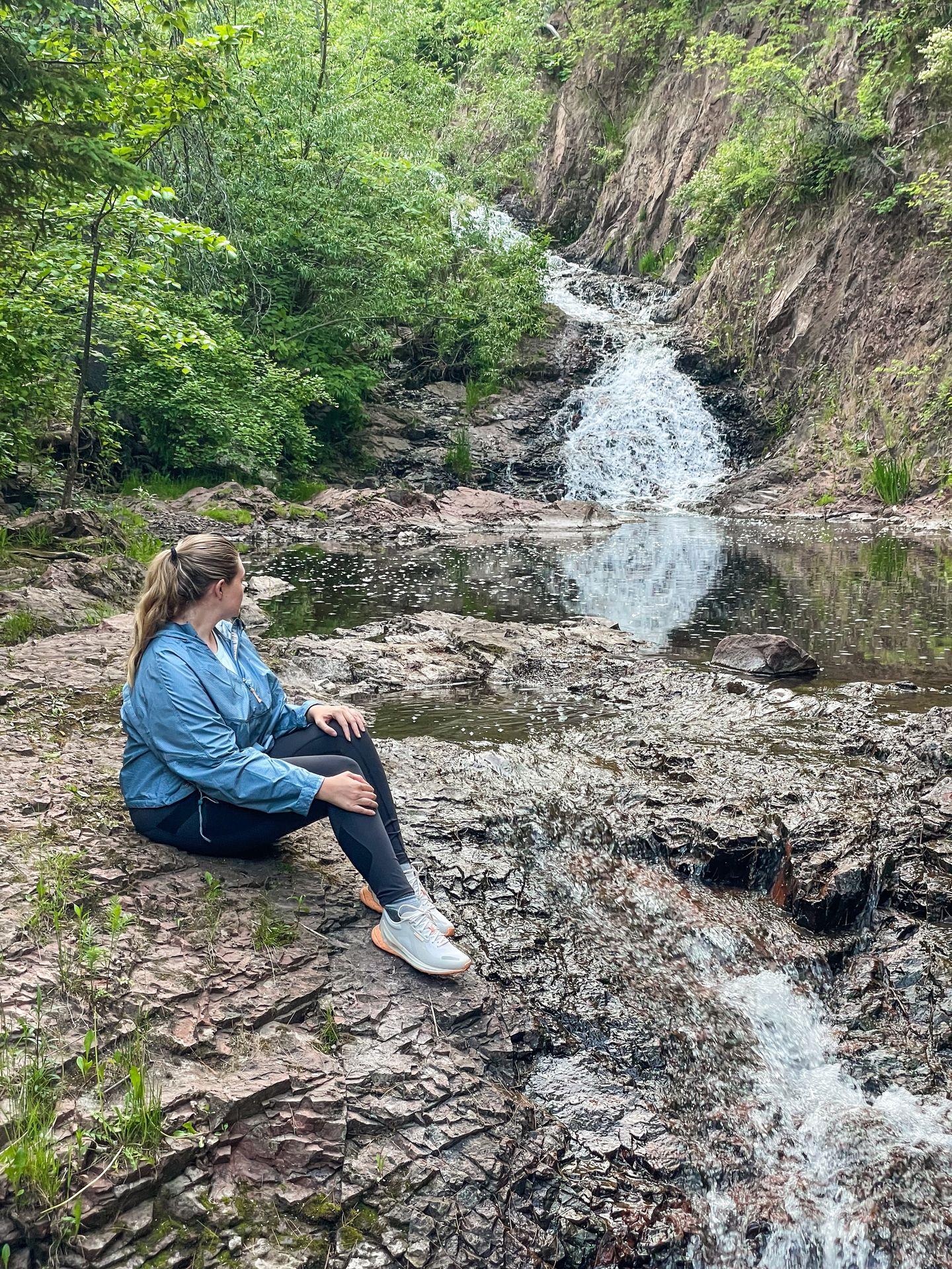 Lydia sitting and looking back at a waterfall in Congdon Park