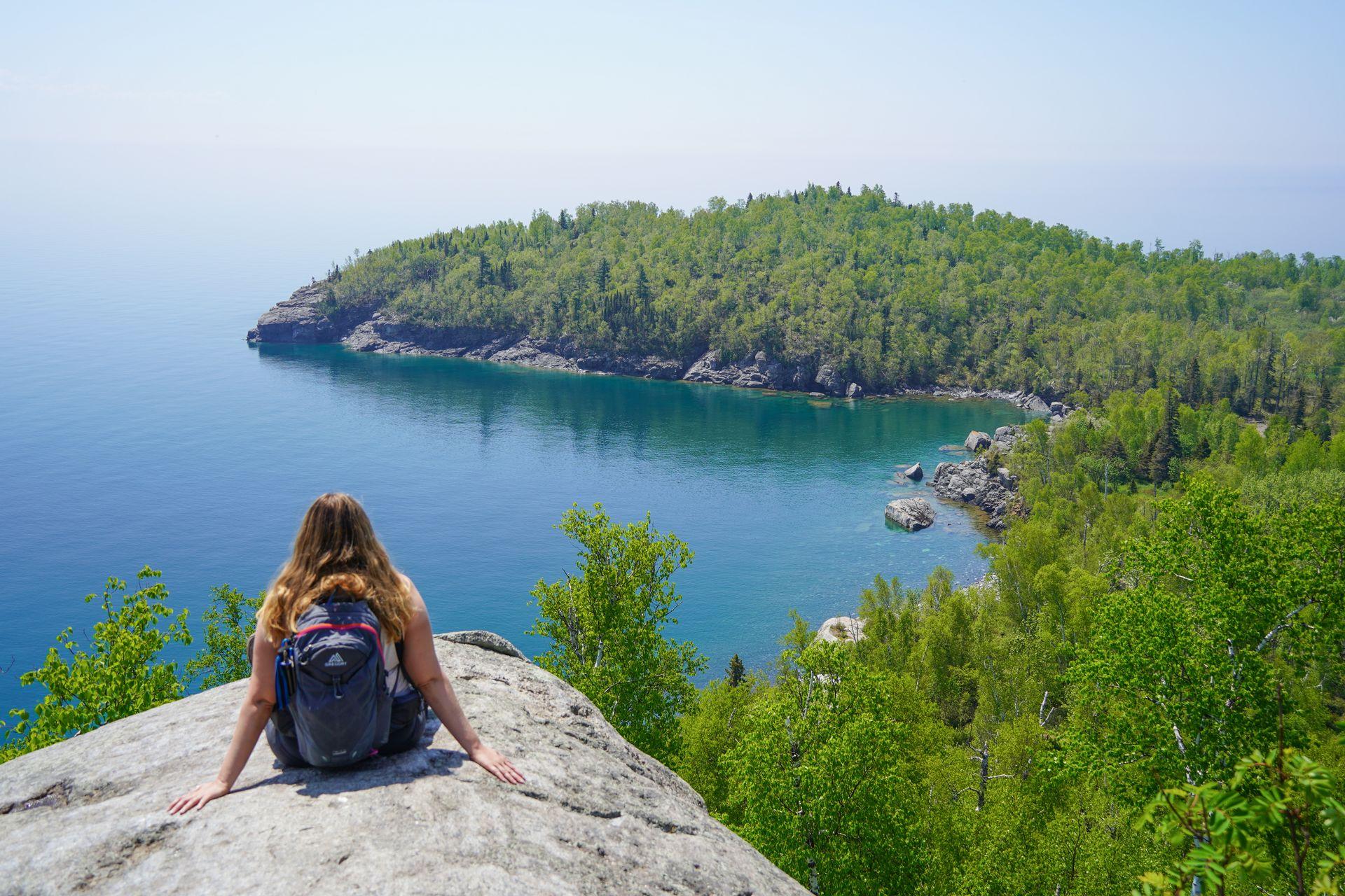 Lydia sitting on a rock and looking out at Lake Superior and a peninsula extending out into the water