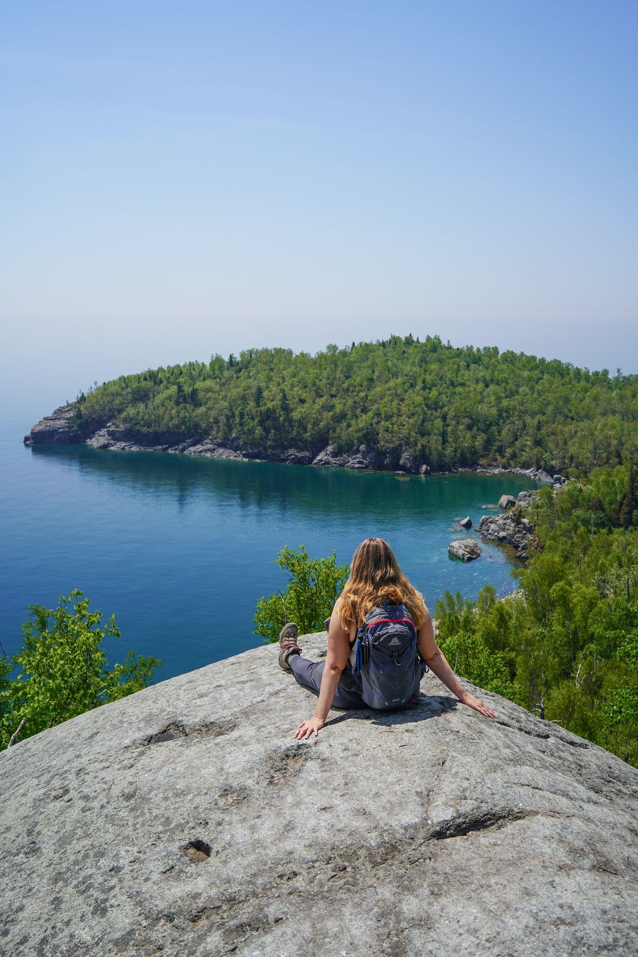 Lydia sitting on a rock and looking out at Lake Superior and a peninsula extending out into the water.