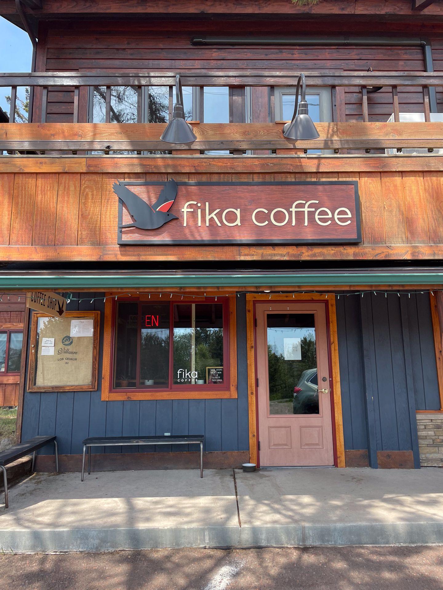 The exterior of Fika Coffee, which has blue paneling and wood surrounded the sign.