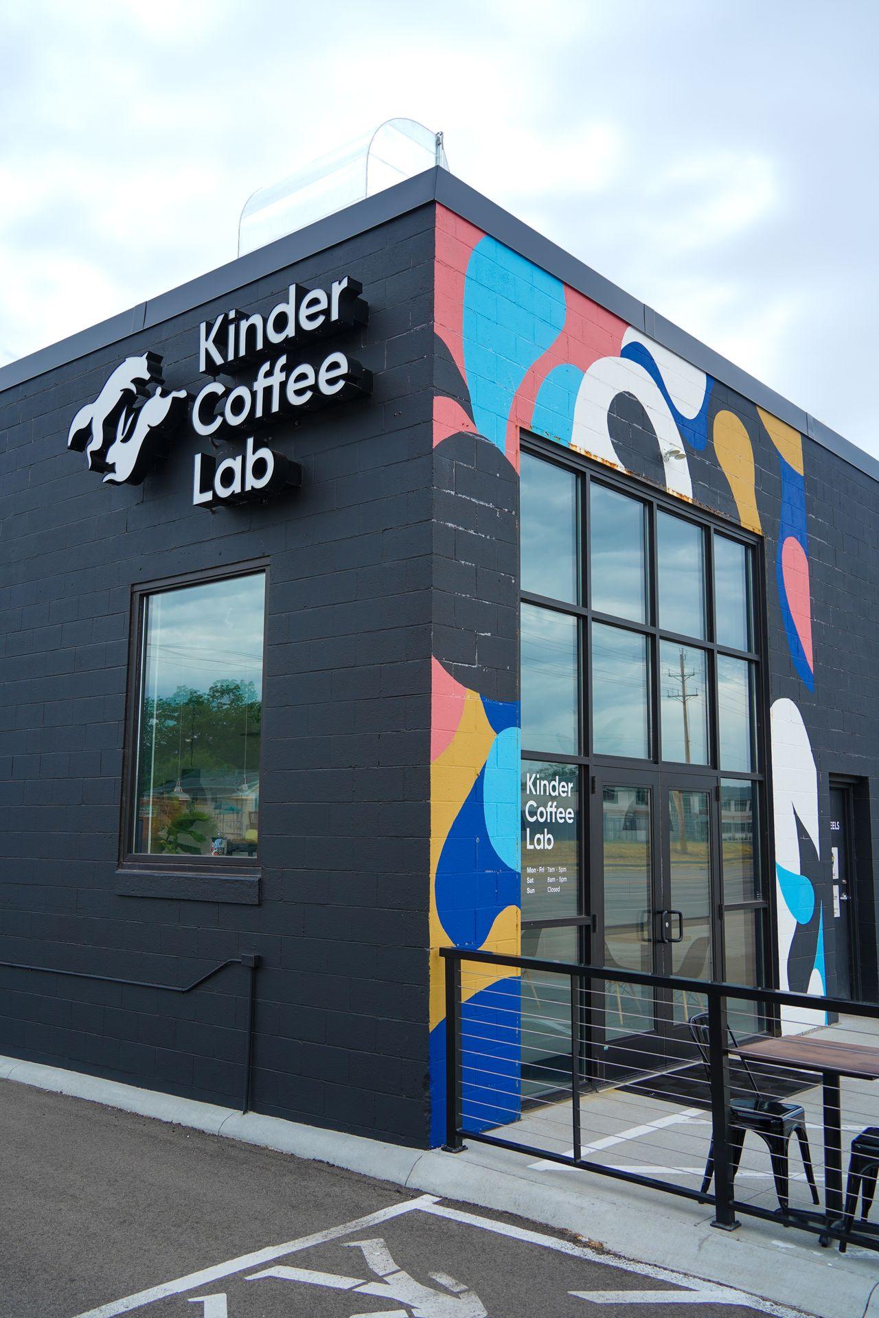 The exterior of Kinder Coffee Lab. The building is black on one side but has an abstract design with blue, yellow, pink and white on the other.