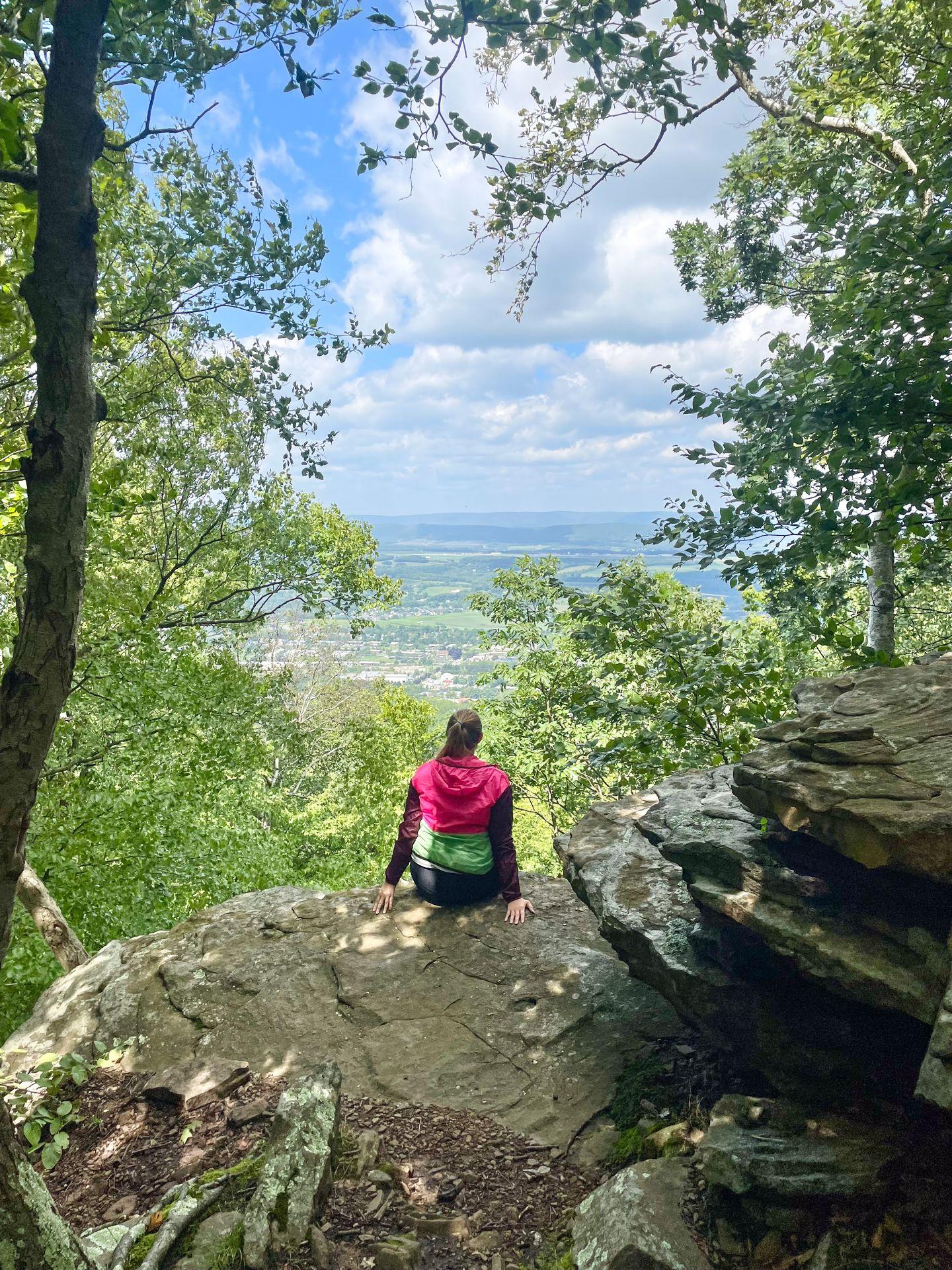 Lydia sitting on a rock and looking out at the view at the Nittany Mall Overlook on the Mount Nittany Loop trail.