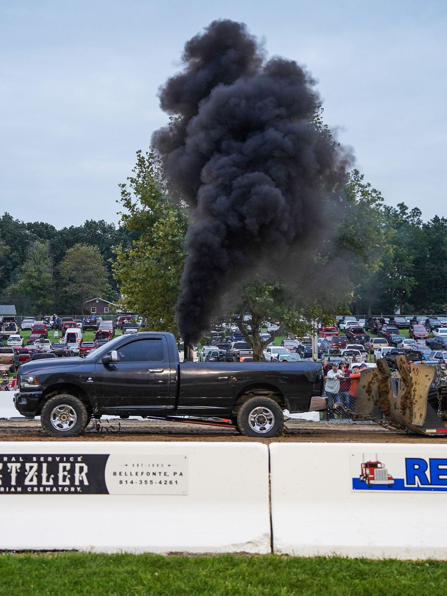 A black pick up truck particpating in the truck pull at the Grange Fair. Black smoke is coming up from the truck.
