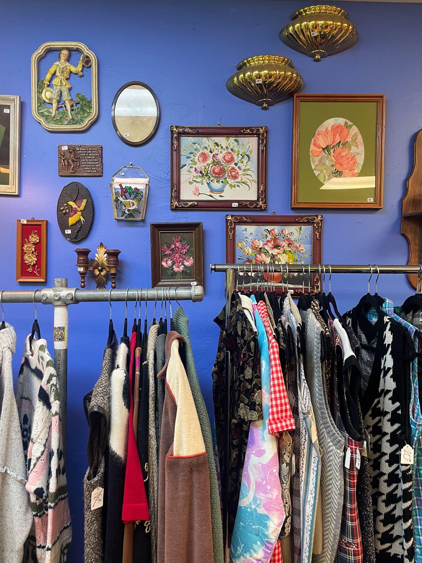 Two racks of vintage clothing. The background wall is blue with artwork hanging.