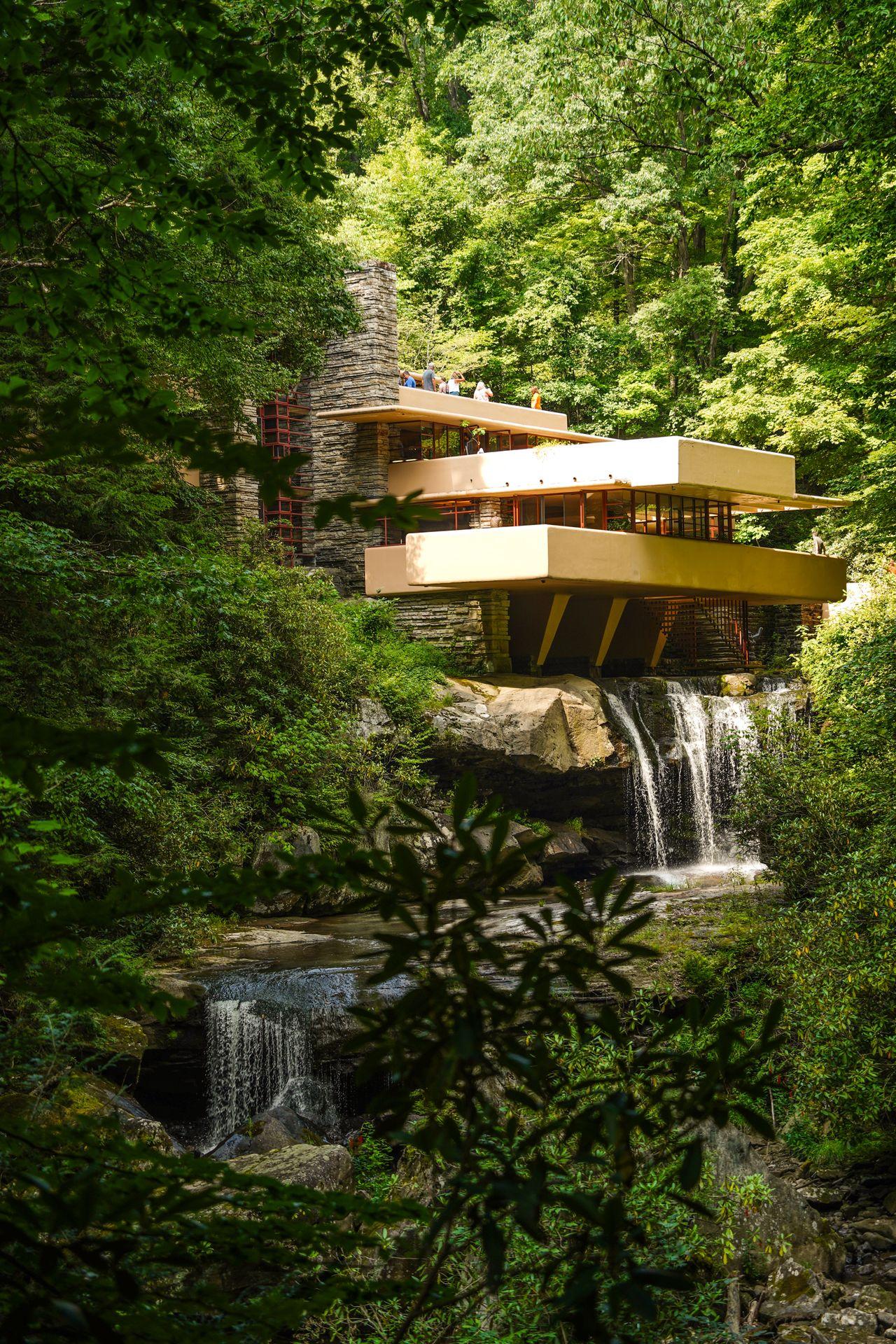 A view of Fallingwater, a brick home with a couple of large balconies. The home is built over a two-layered waterfall.