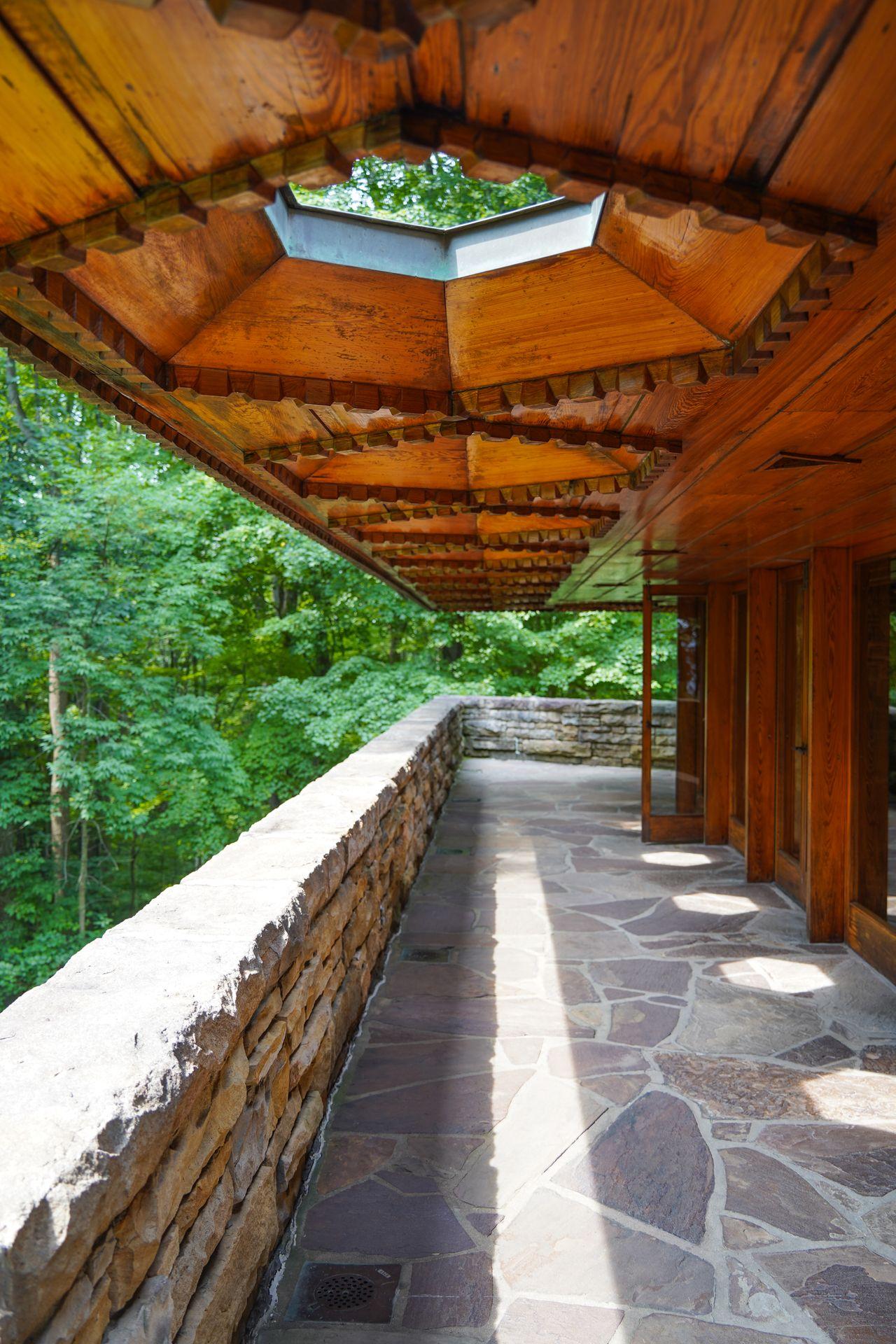 The outdoor balcony at Kentuck Knob. There is a stone walkway and a brown roof area with hexagon shapes letting in light.