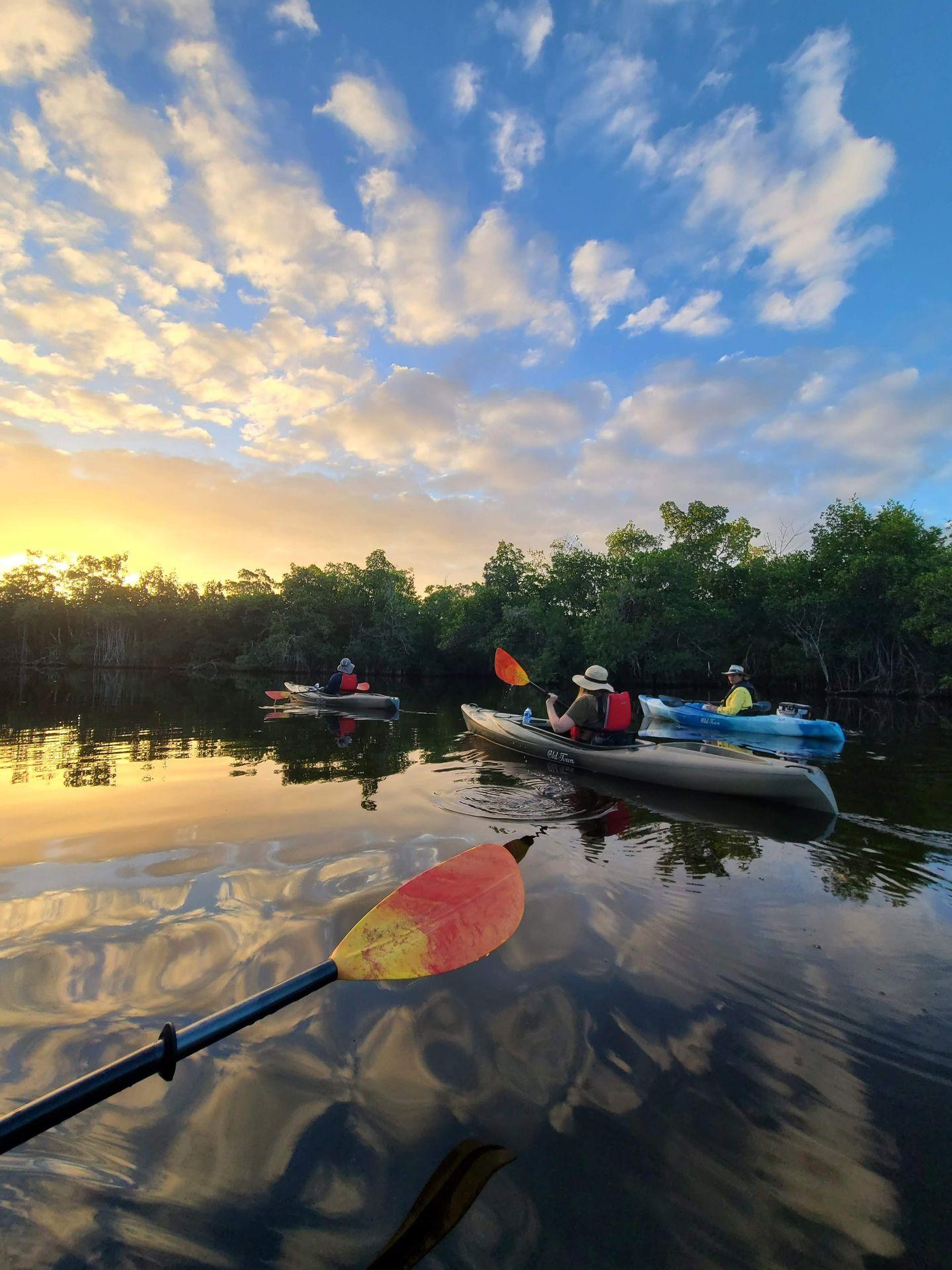 3 people kayaking at sunrise.