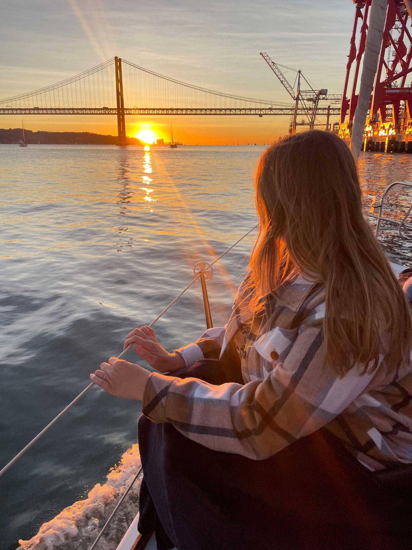Lydia watching the sunset from a boat. There is a bridge in the distance.