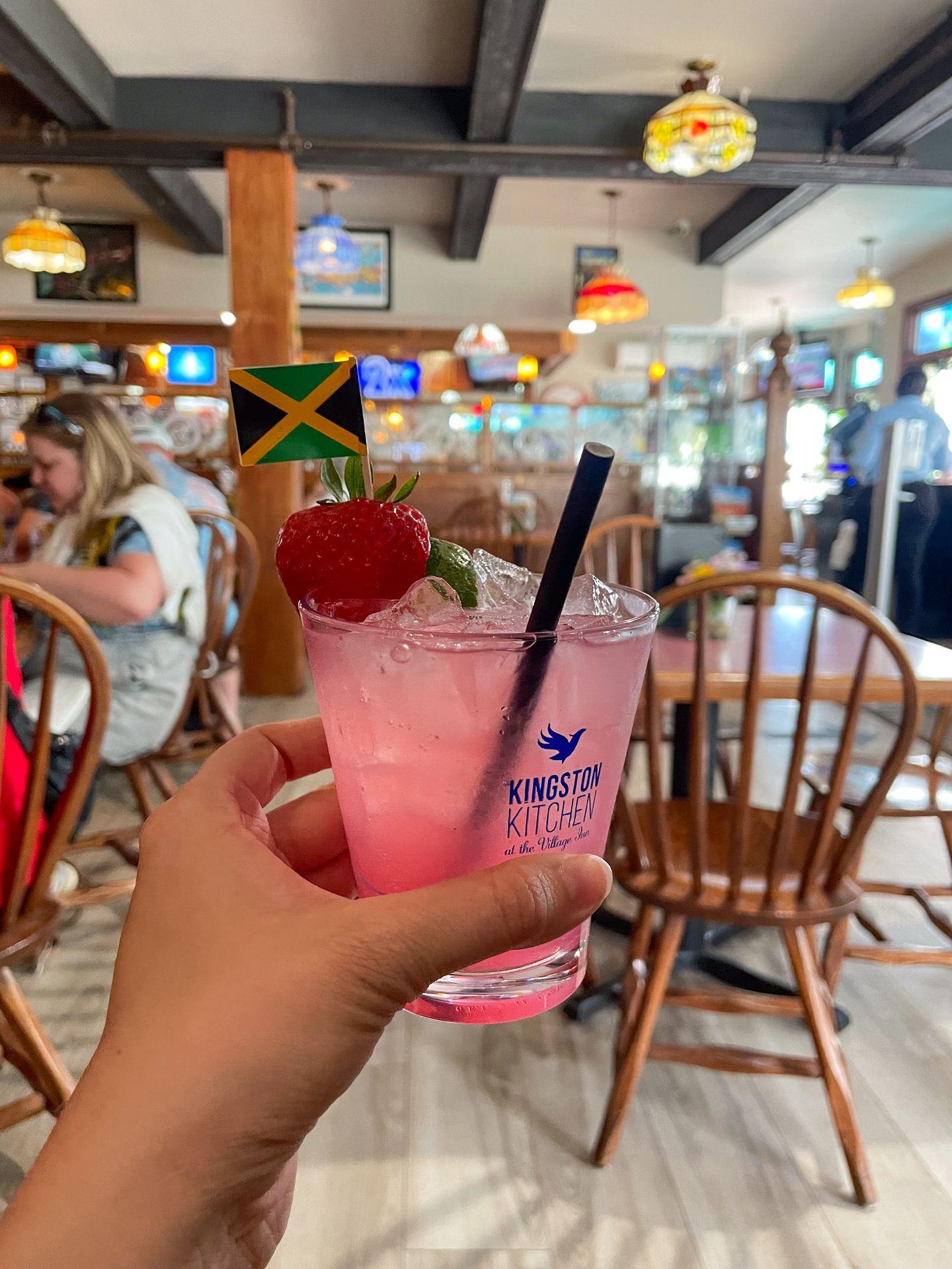 Holding up a pink cocktail with a Jamaican flag sticking out of it