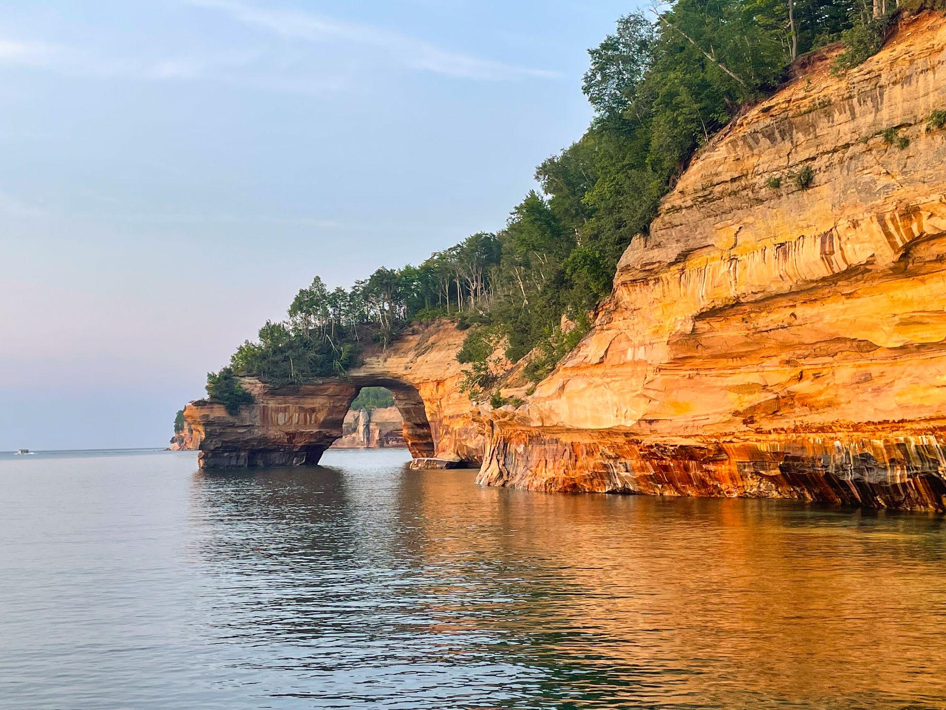 Lover's Leap Arch seen from a boat and glowing orange at golden hour.