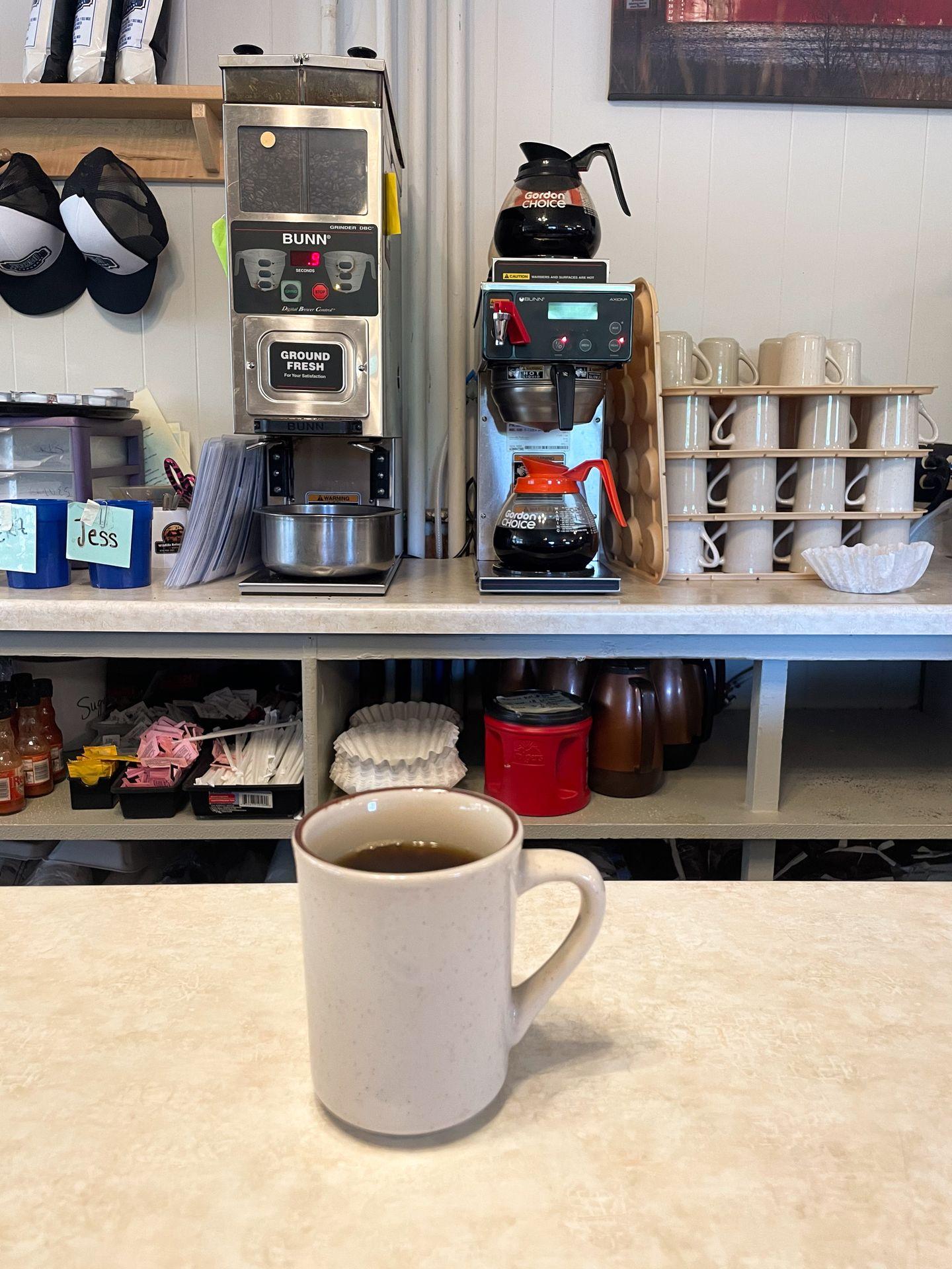 A cup of coffee sitting on a bar and a coffee machine behind the counter