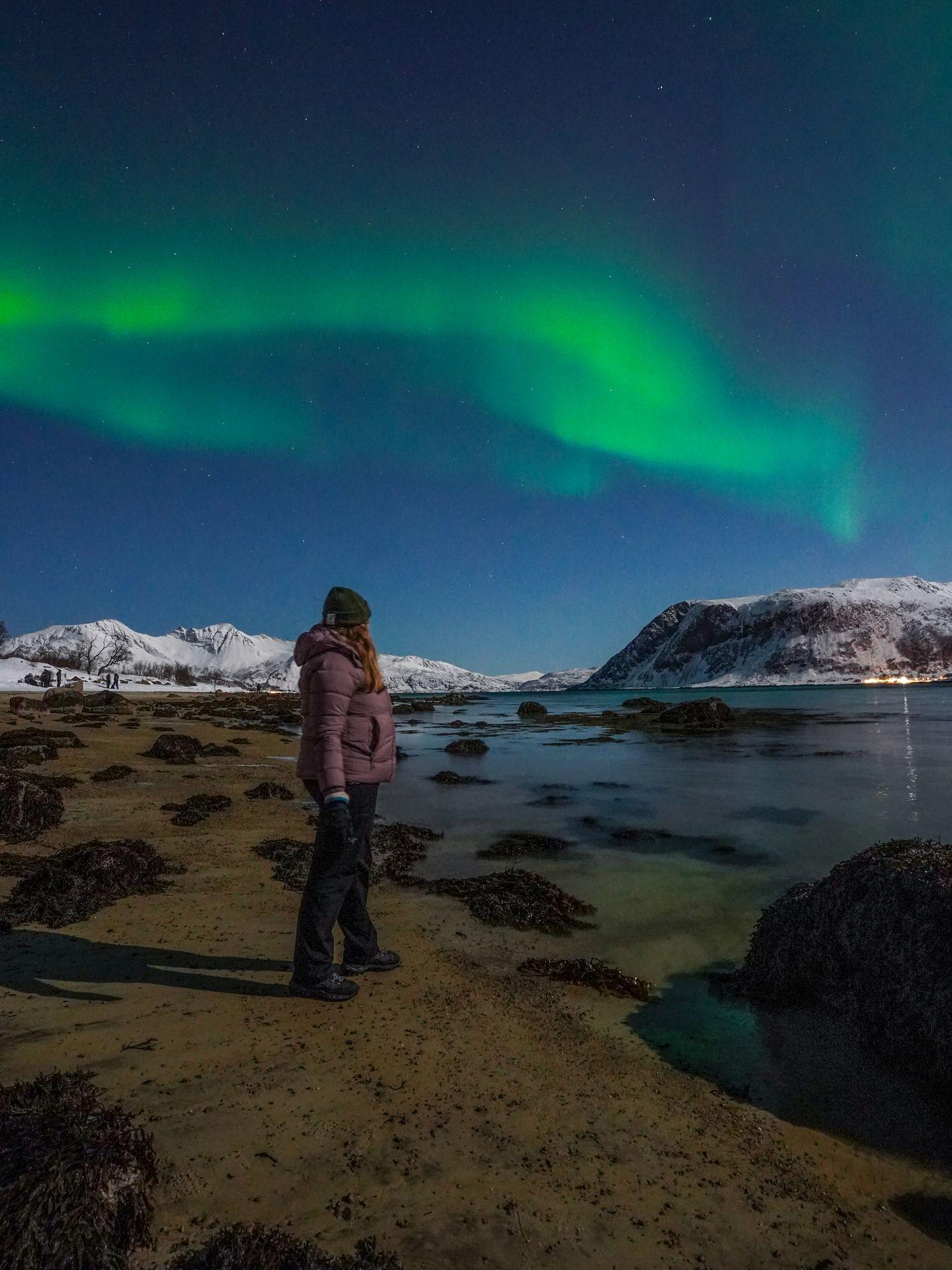 Looking standing on a beach and looking back at the Northern Lights in the distance.