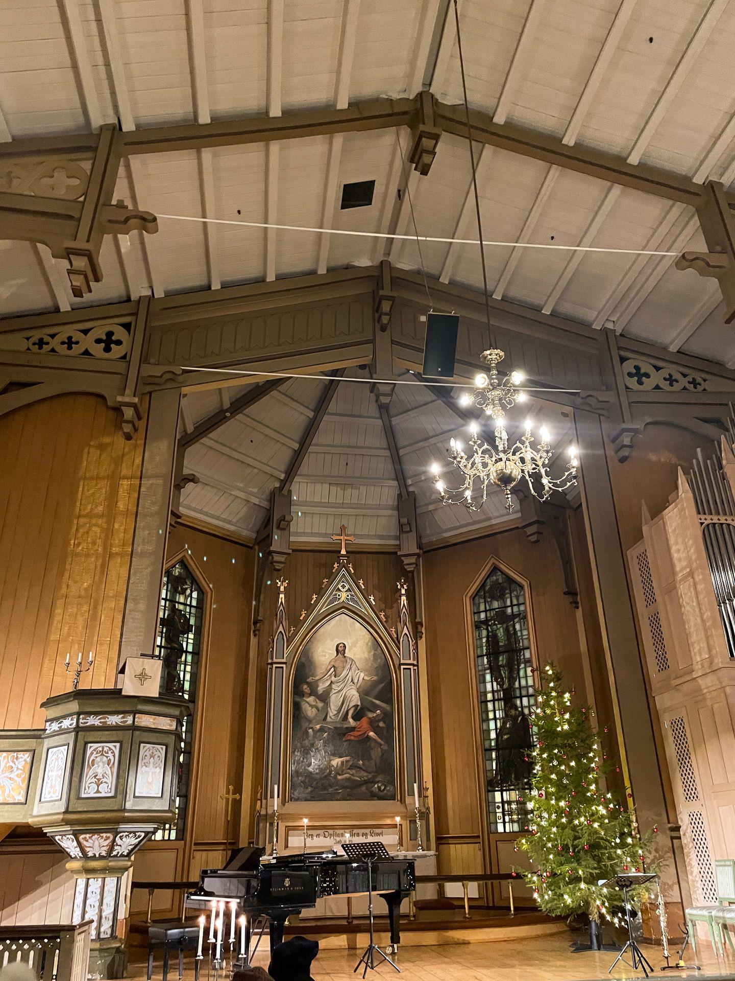 Inside of the Tromso Cathedral. There is religious artwork, a chandelier and a Christmas tree