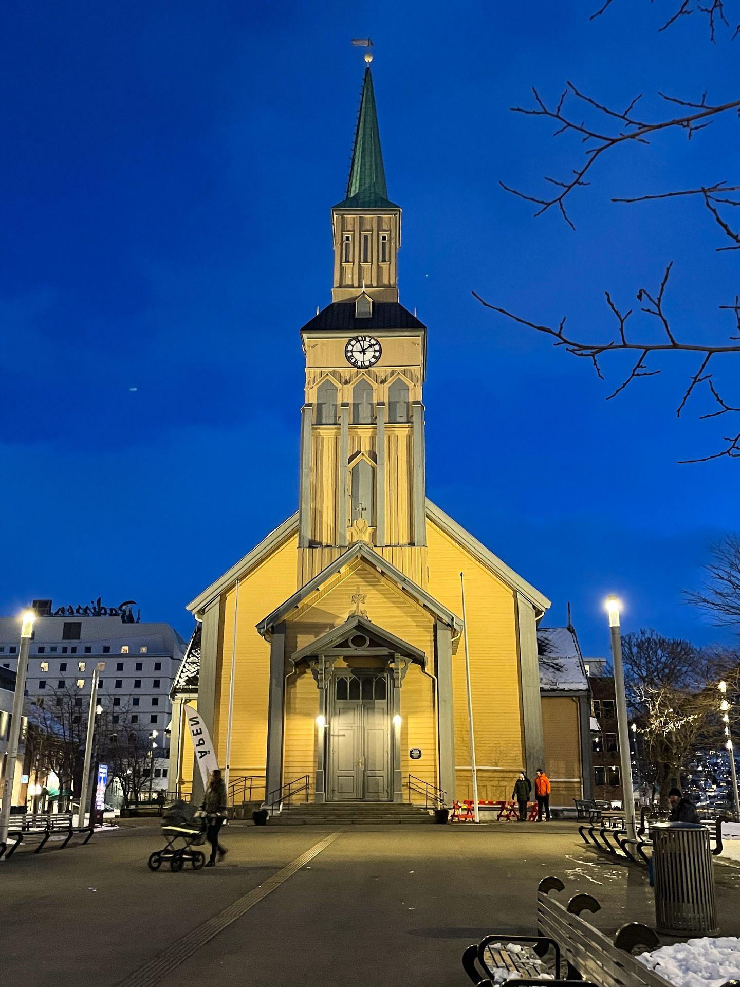The exterior of the Tromso Cathedral, a yellow building with a tall tower