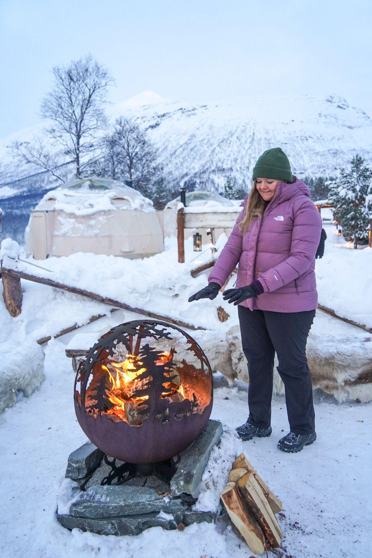 Lydia warming her hands at a campfire at Camp Tamok, which is the same property as the Tromso Ice Domes